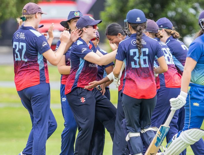 Softball team in blue and red uniforms huddles on the field, celebrating together with gloves and bats nearby