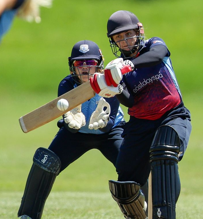 Two cricket players in dark uniforms, one batting and one catching, during a match outdoors