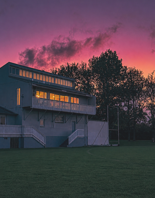 Building at sunset with lit windows and a vivid pink-purple sky behind silhouetted trees