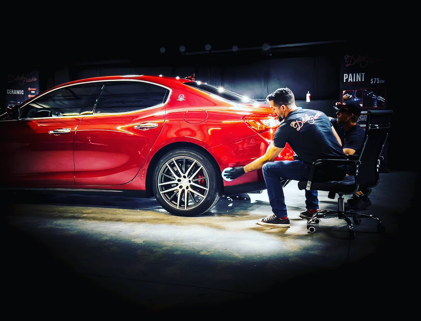 A man is sitting in a chair next to a red car.