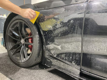A person is applying a protective film to the side of a car.