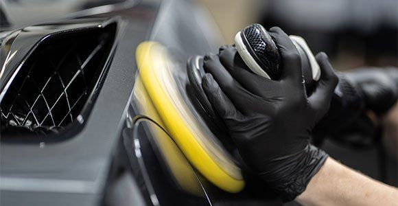 A person wearing black gloves is polishing a car.