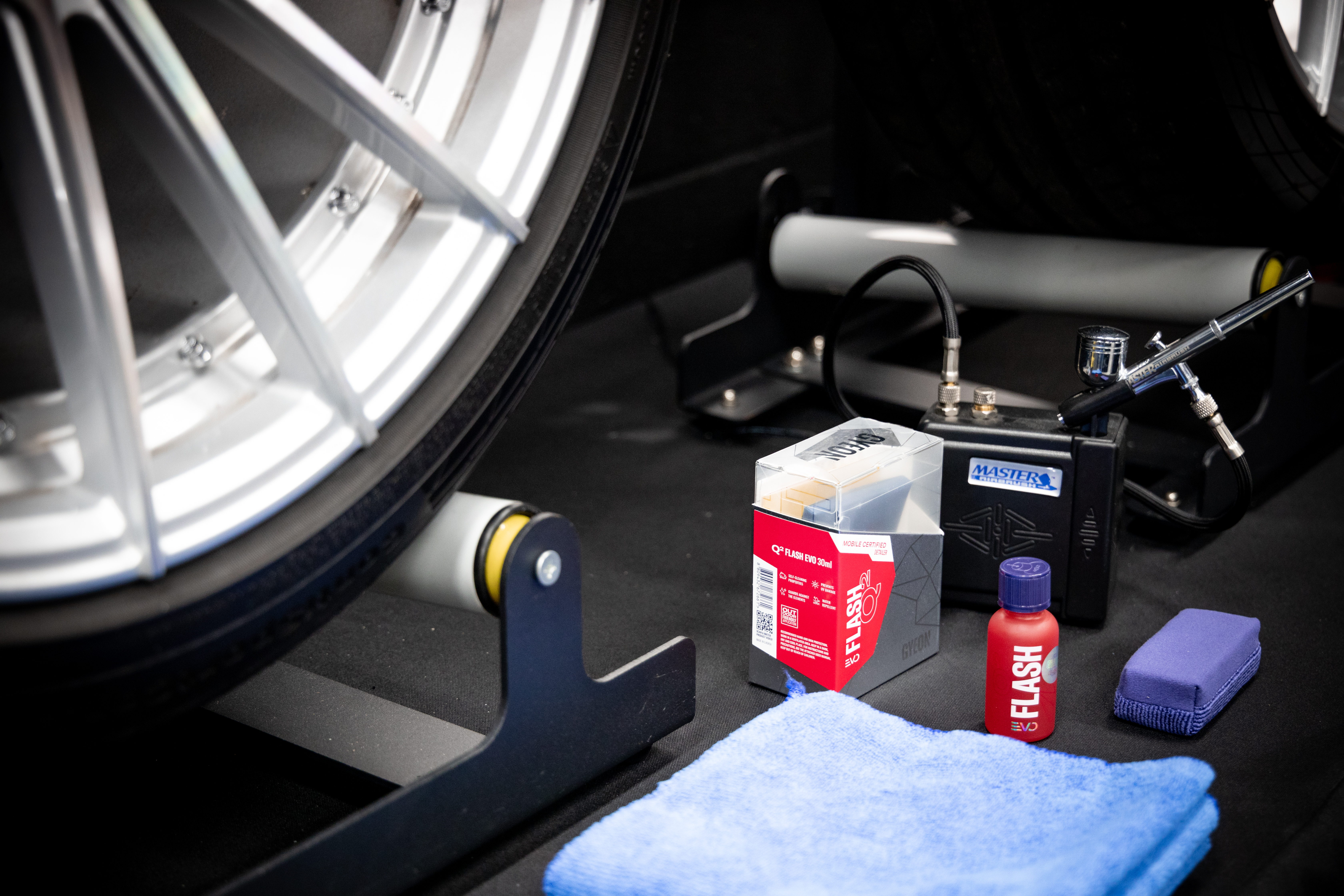 A car wheel is sitting on a table next to a bottle of flash and a blue towel.