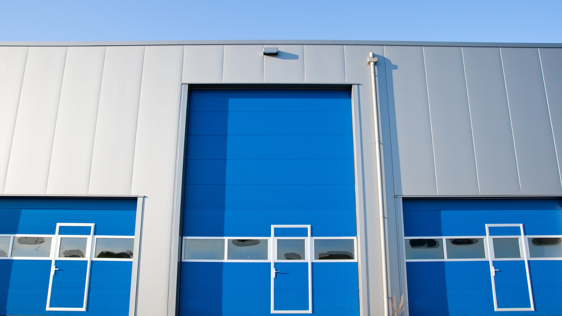 Blue industrial doors on a silver building under a clear sky.