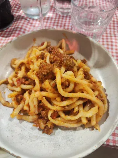 Piatto di pasta con sugo di carne in una ciotola bianca, su una tovaglia a quadri rossi e bianchi.