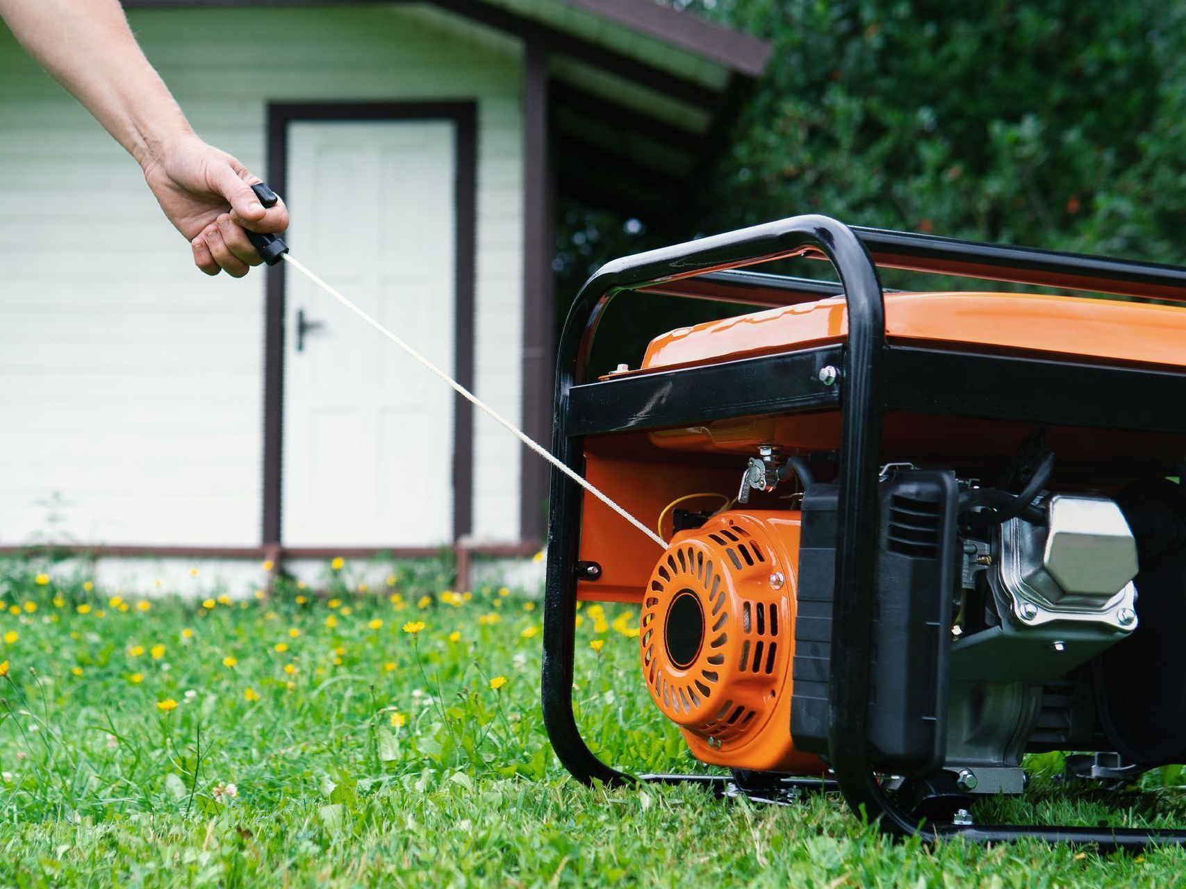a person is starting a generator in the grass in front of a house .