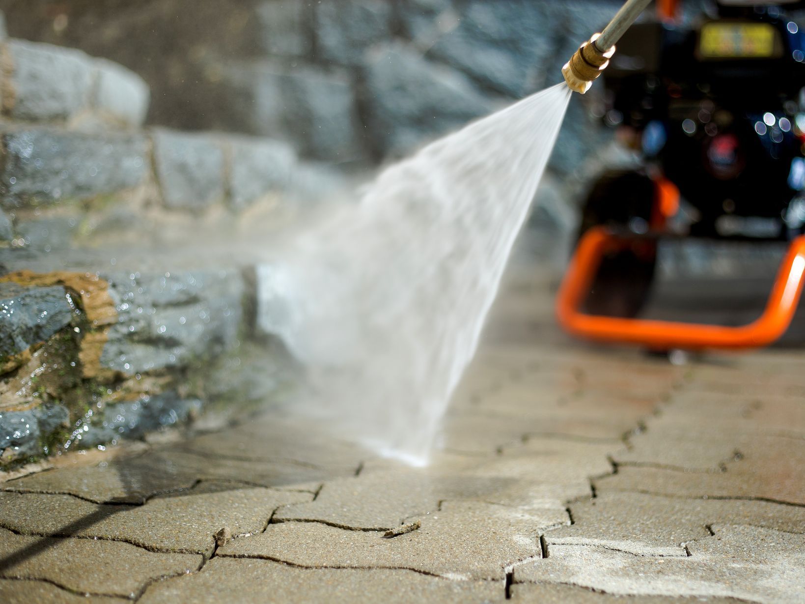 a person is using a high pressure washer to clean a brick walkway .