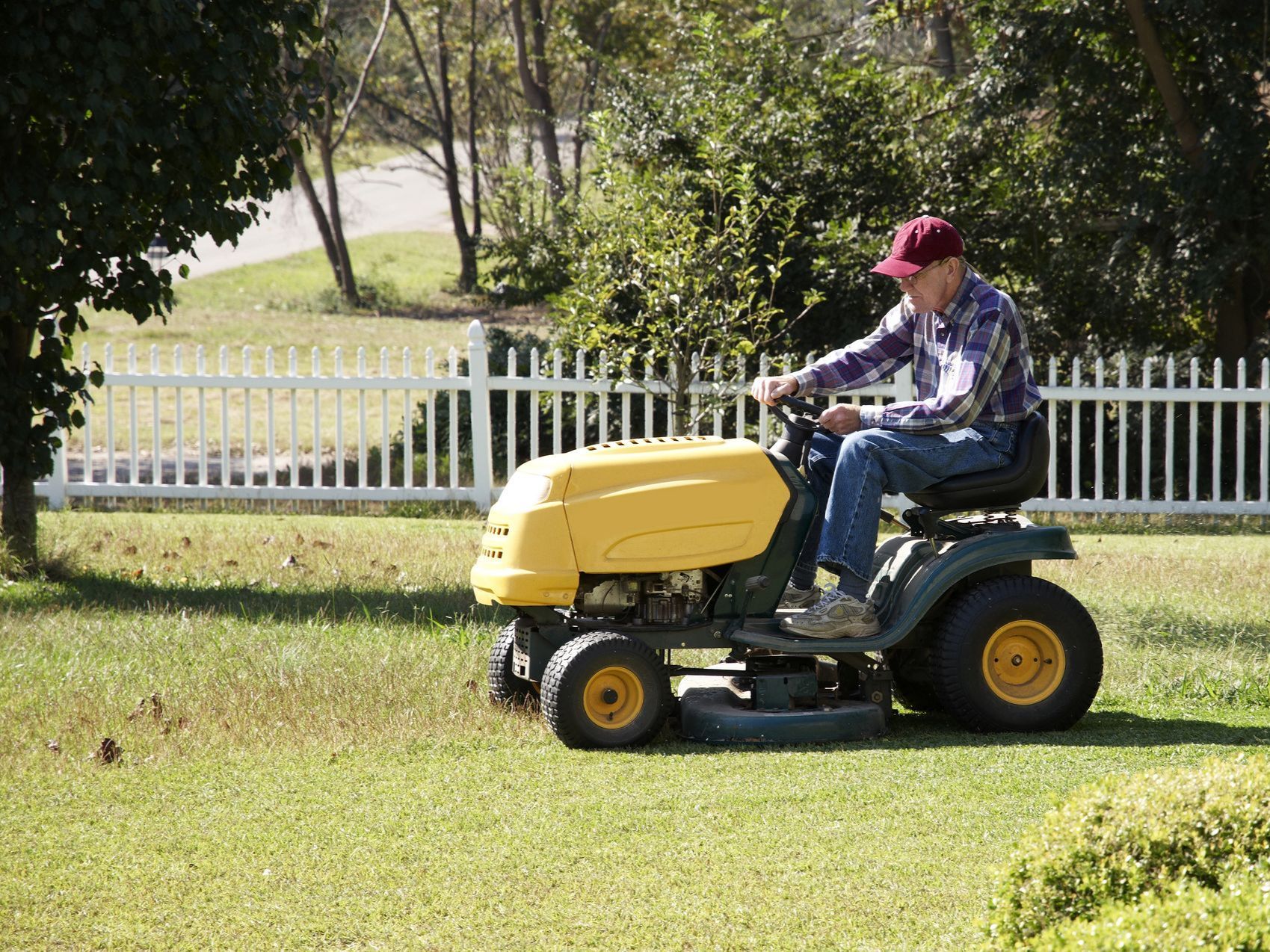 a man is riding a yellow lawn mower in front of a white picket fence .