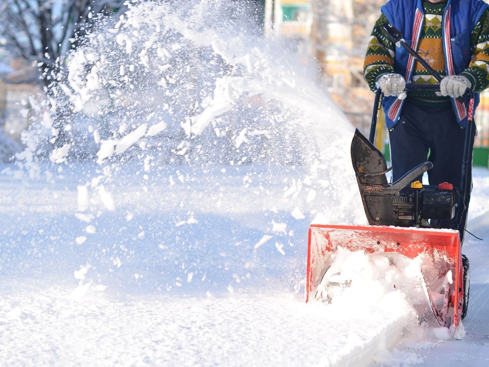 a man is using a snow blower to remove snow from the sidewalk .