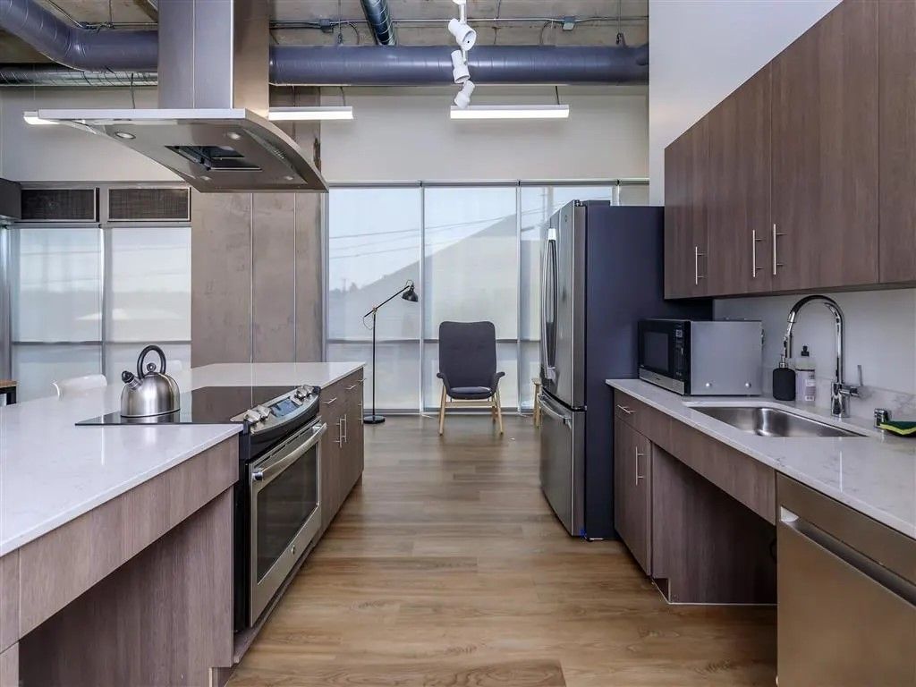 Modern kitchen with wooden cabinets, stainless steel appliances, and large windows.