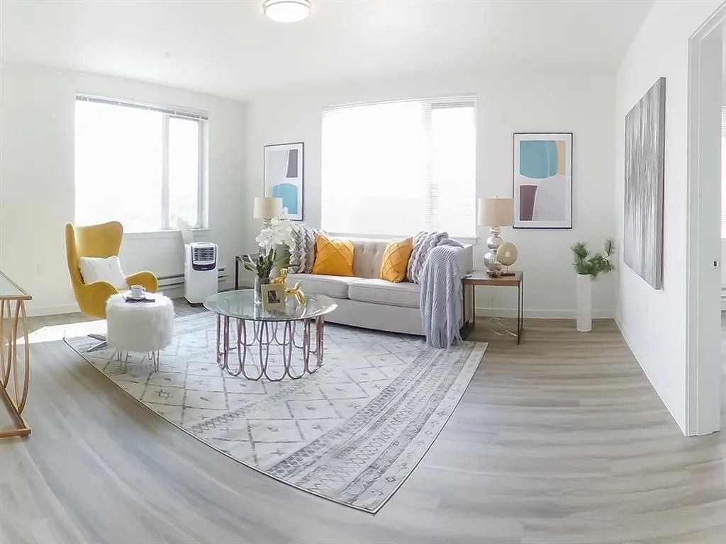 Living room with light-colored sofa, rug, and accent chairs, near large windows and art.
