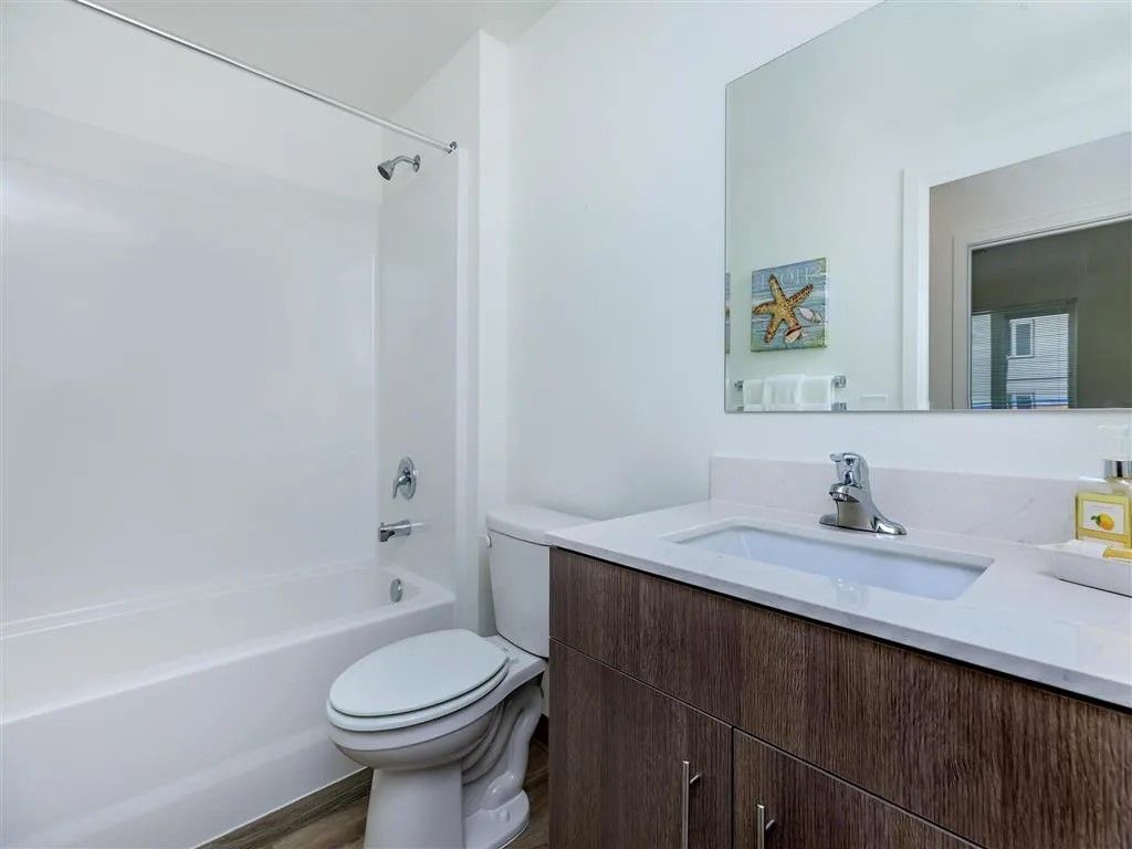 A modern bathroom with a white tub, toilet, and vanity with a dark wood cabinet.