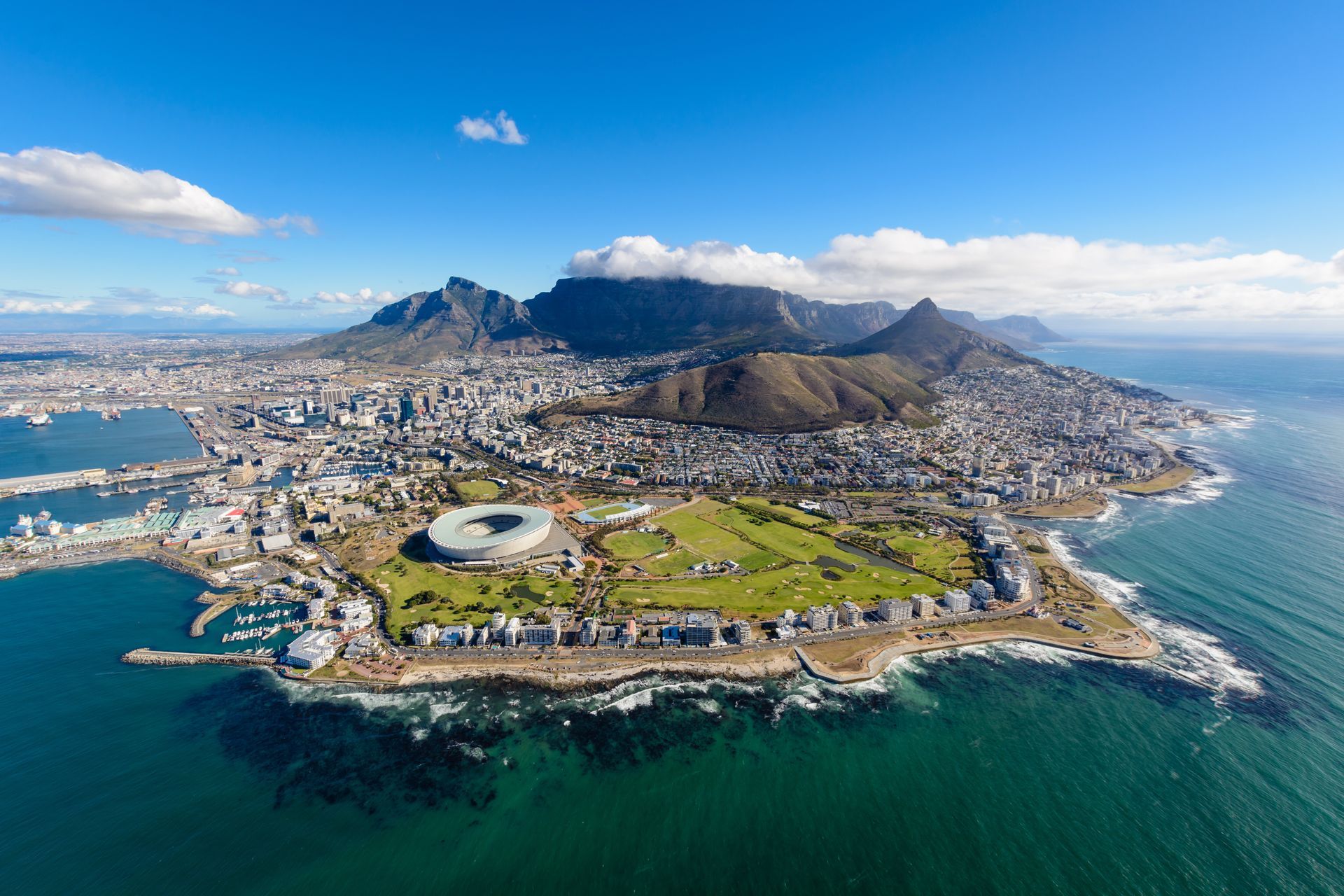 Aerial view of Cape Town, South Africa, featuring Table Mountain, the coastline, and the Cape Town Stadium.