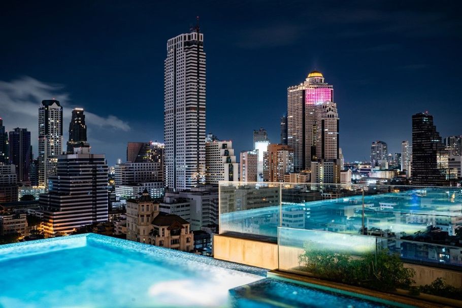 City skyline at night seen from a rooftop pool with glowing blue water and glass railing