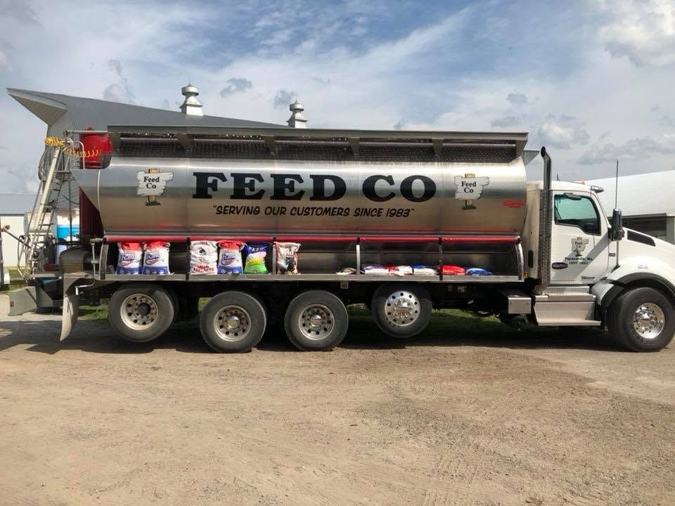White FEED CO grain truck parked on dirt lot under a cloudy sky