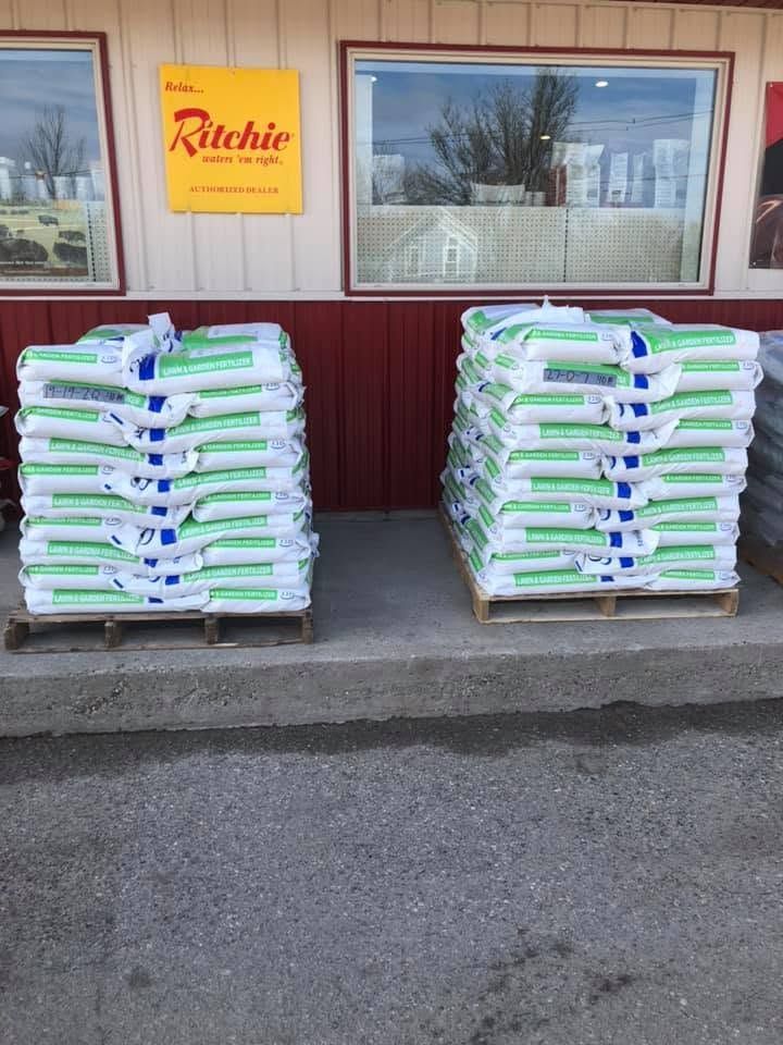 Two stacked pallets of bagged material outside a building with a yellow sign and window.