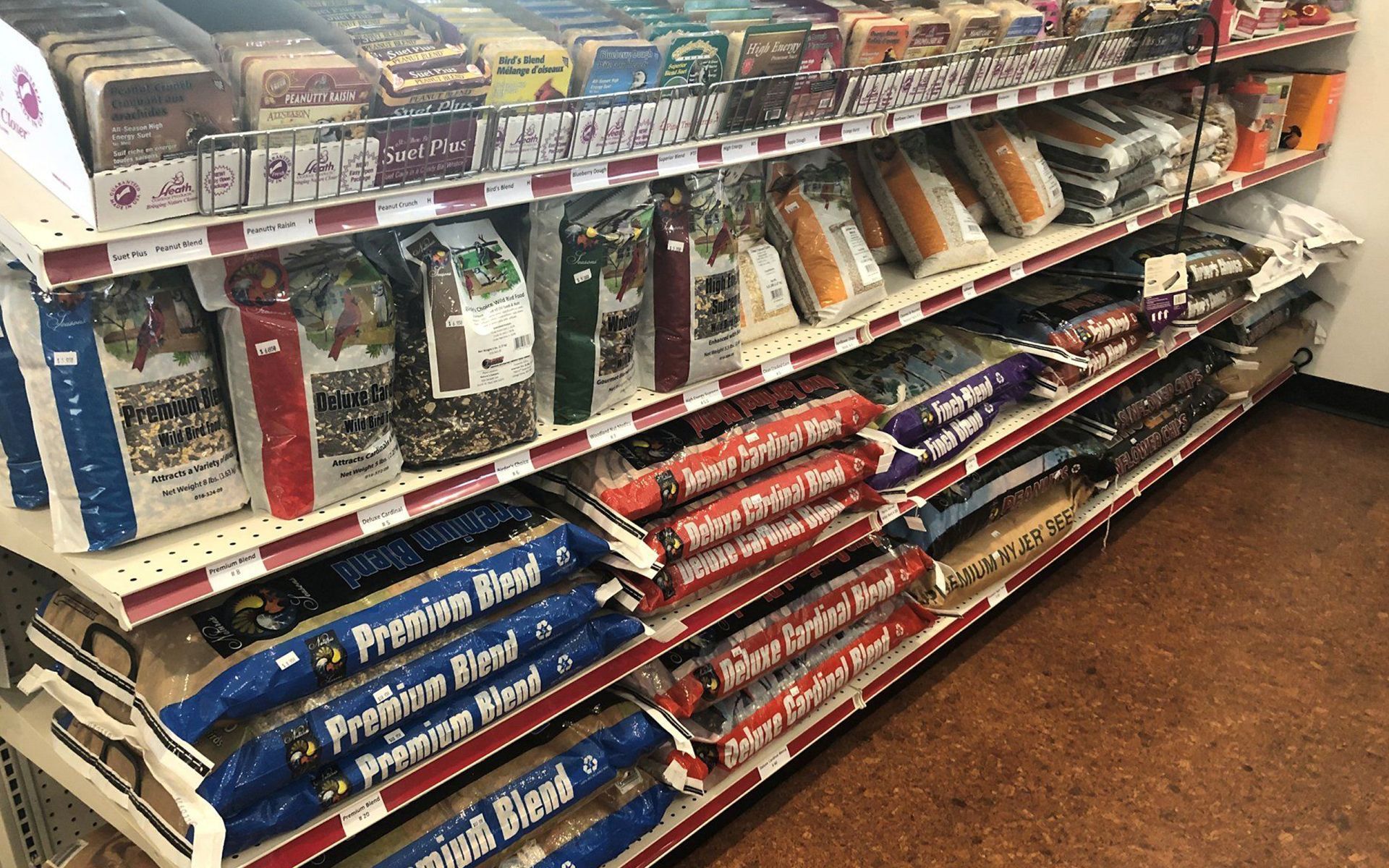 Pet store aisle with stacked pet food bags and supplies on white shelves and brown floor