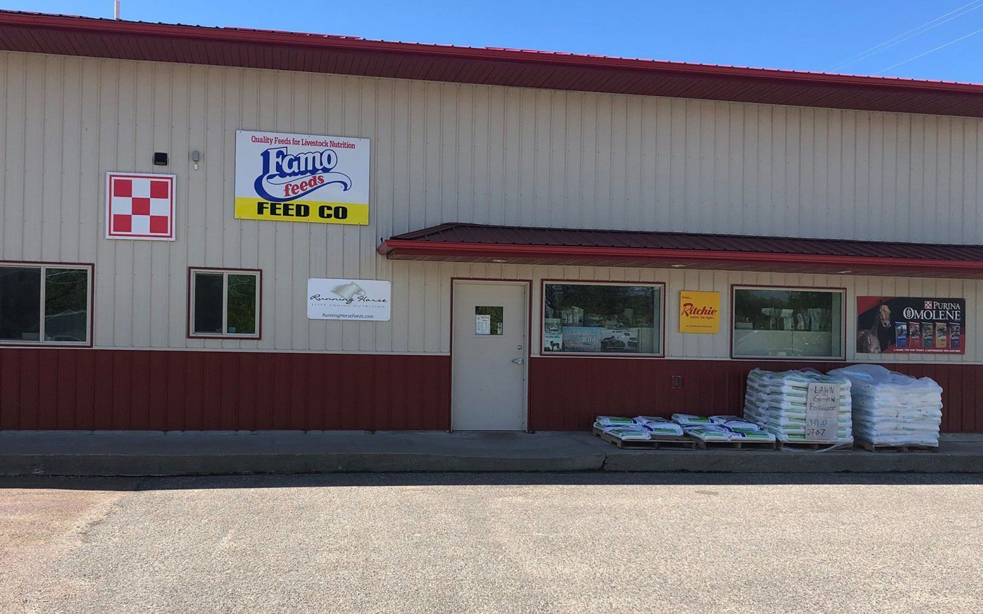 Small storefront with red trim, signs, a white door, and stacked bags outside.