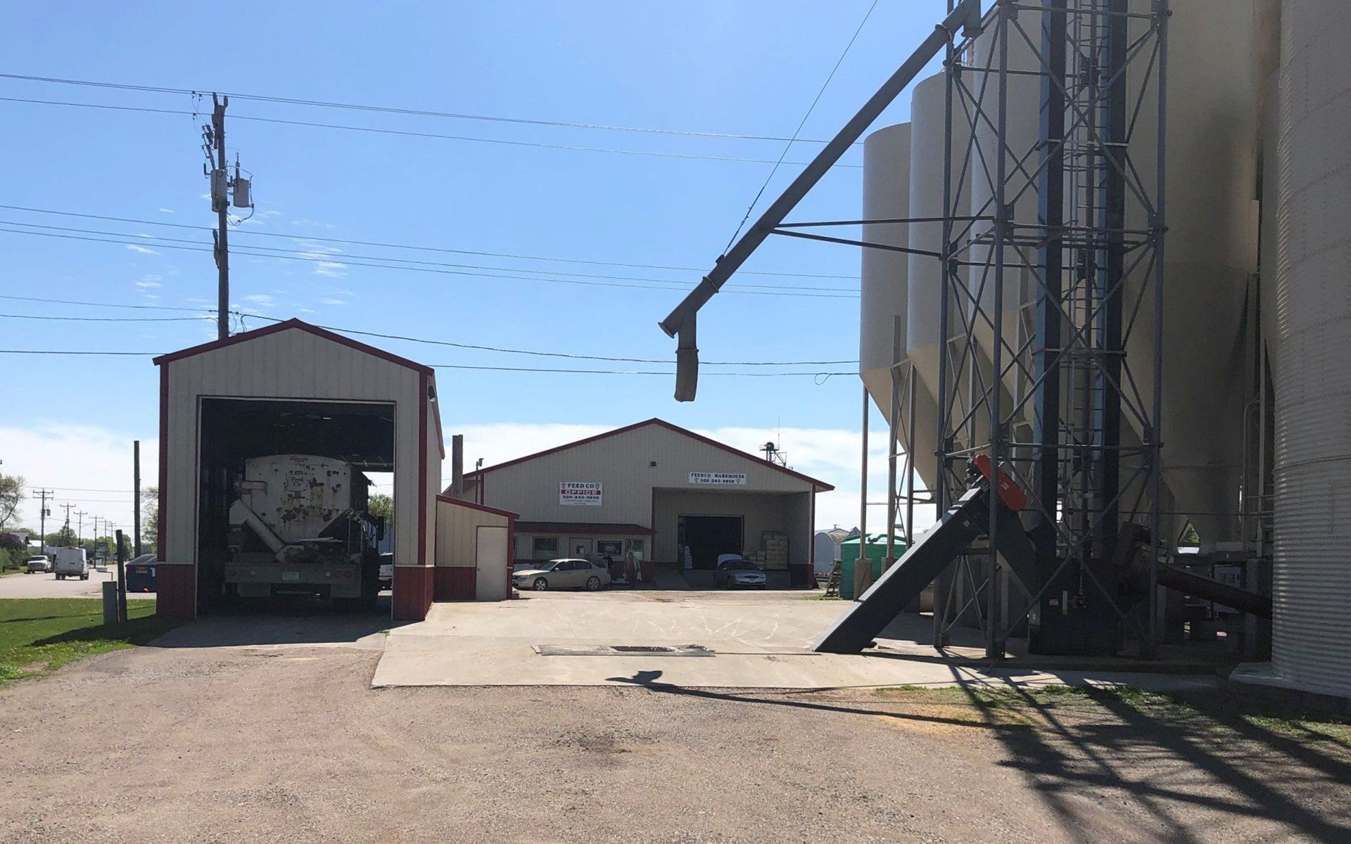 Industrial yard with grain silos, warehouses, and a covered loading area under a clear blue sky