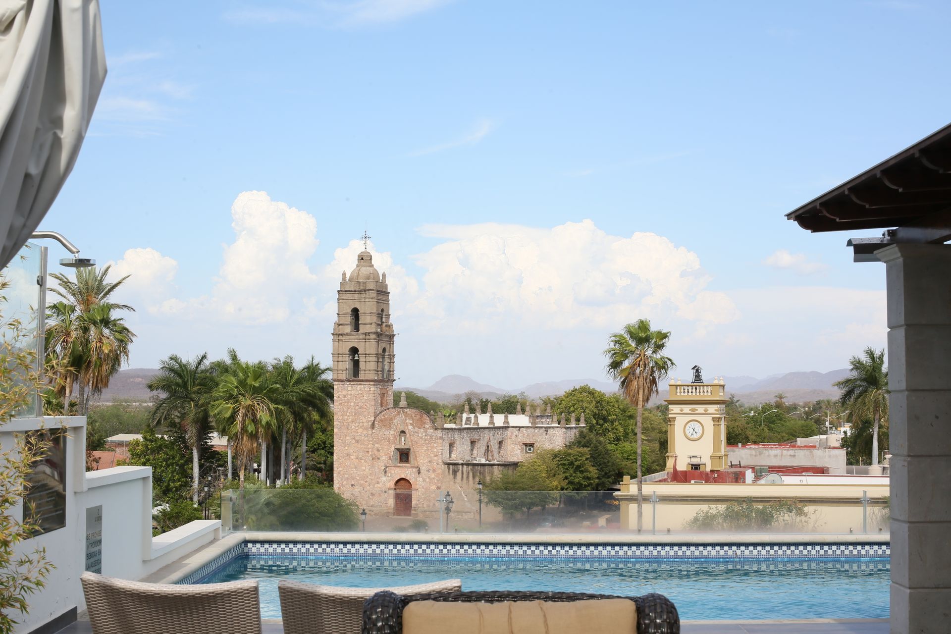 Una vista de una ciudad desde una piscina en la azotea con una torre de reloj al fondo.