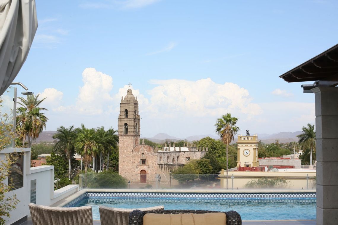 Una vista de una ciudad desde una piscina en la azotea con una torre de reloj al fondo.