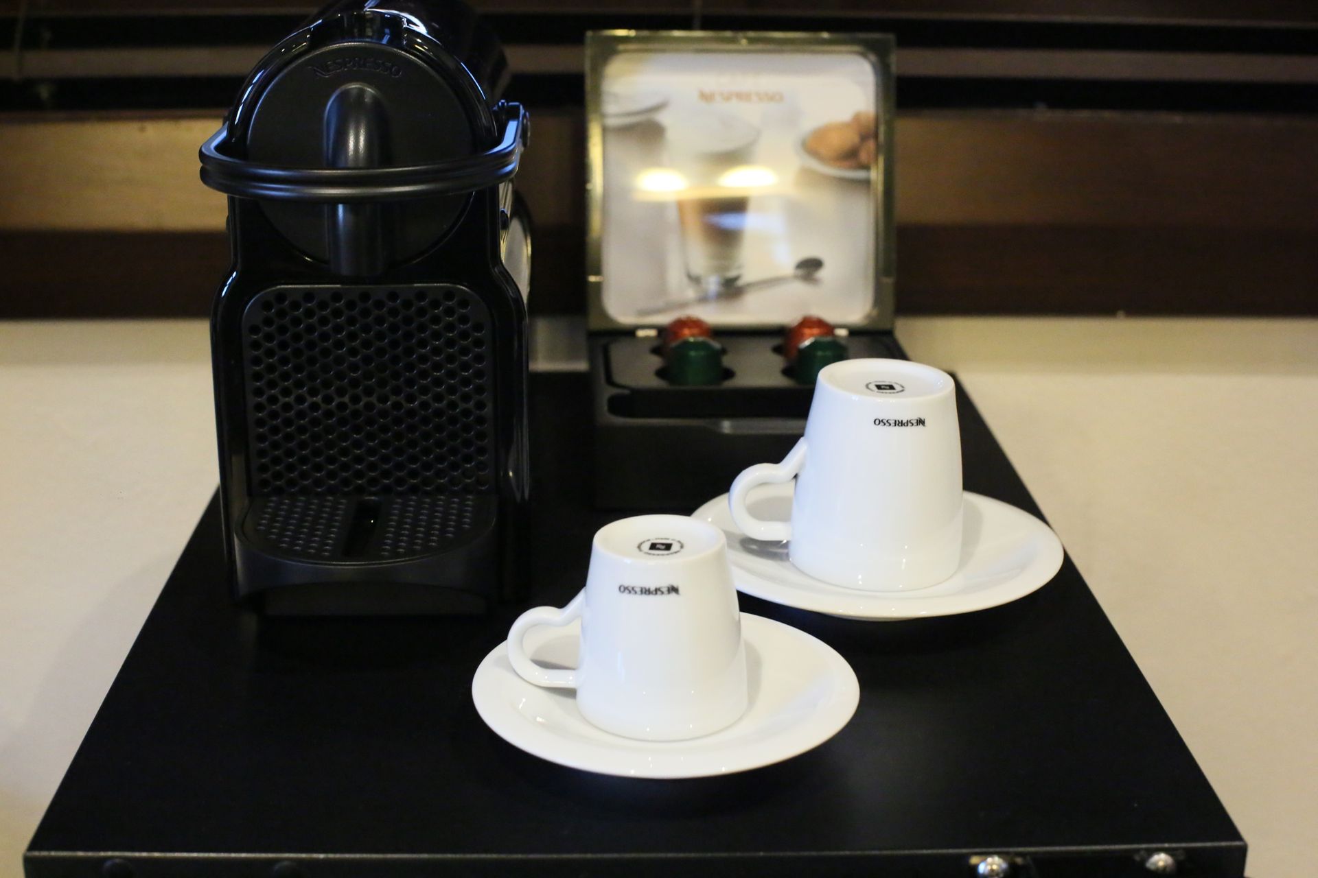 Two cups and saucers on a table next to a coffee machine