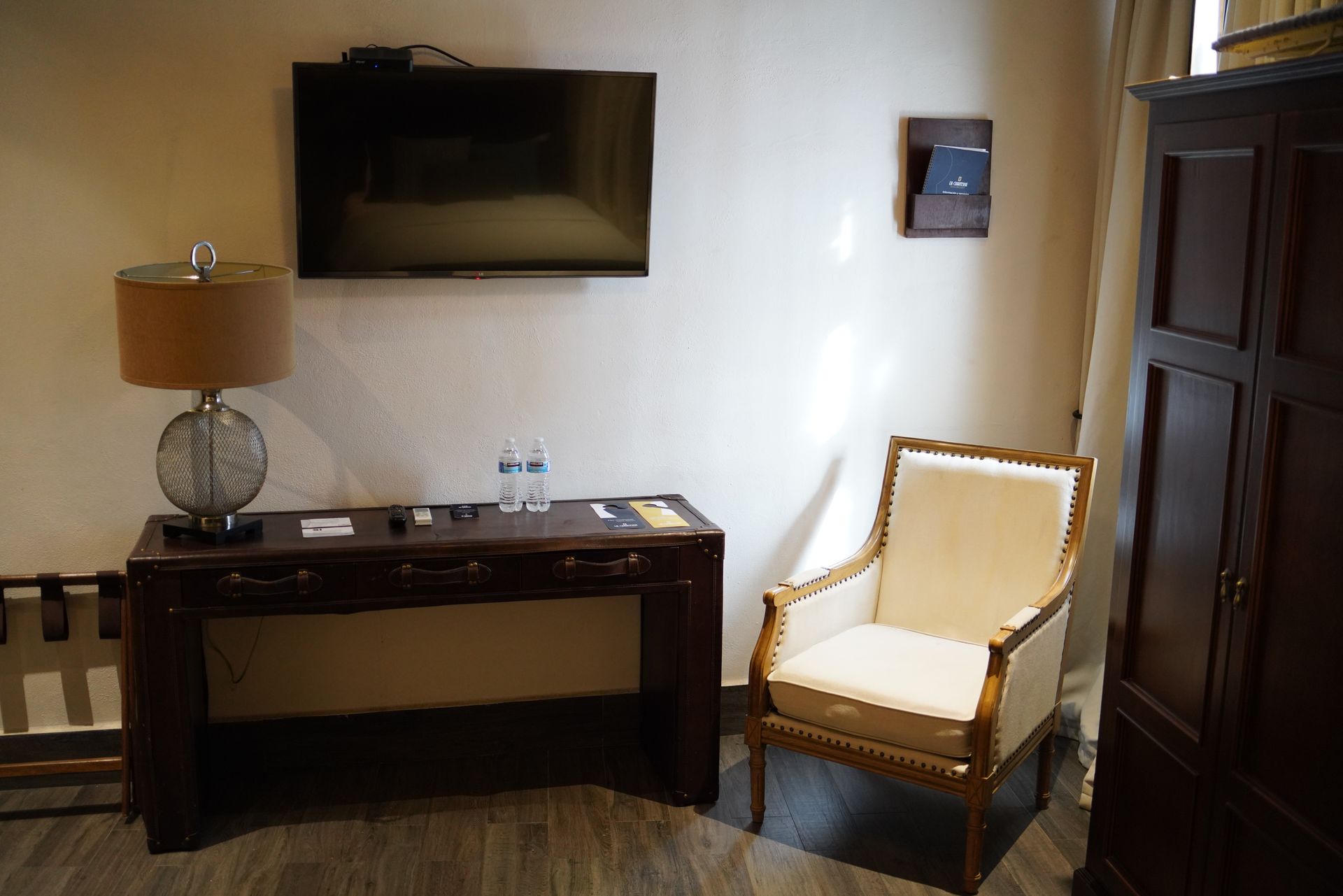 A hotel room with a chair , desk , television and lamp.