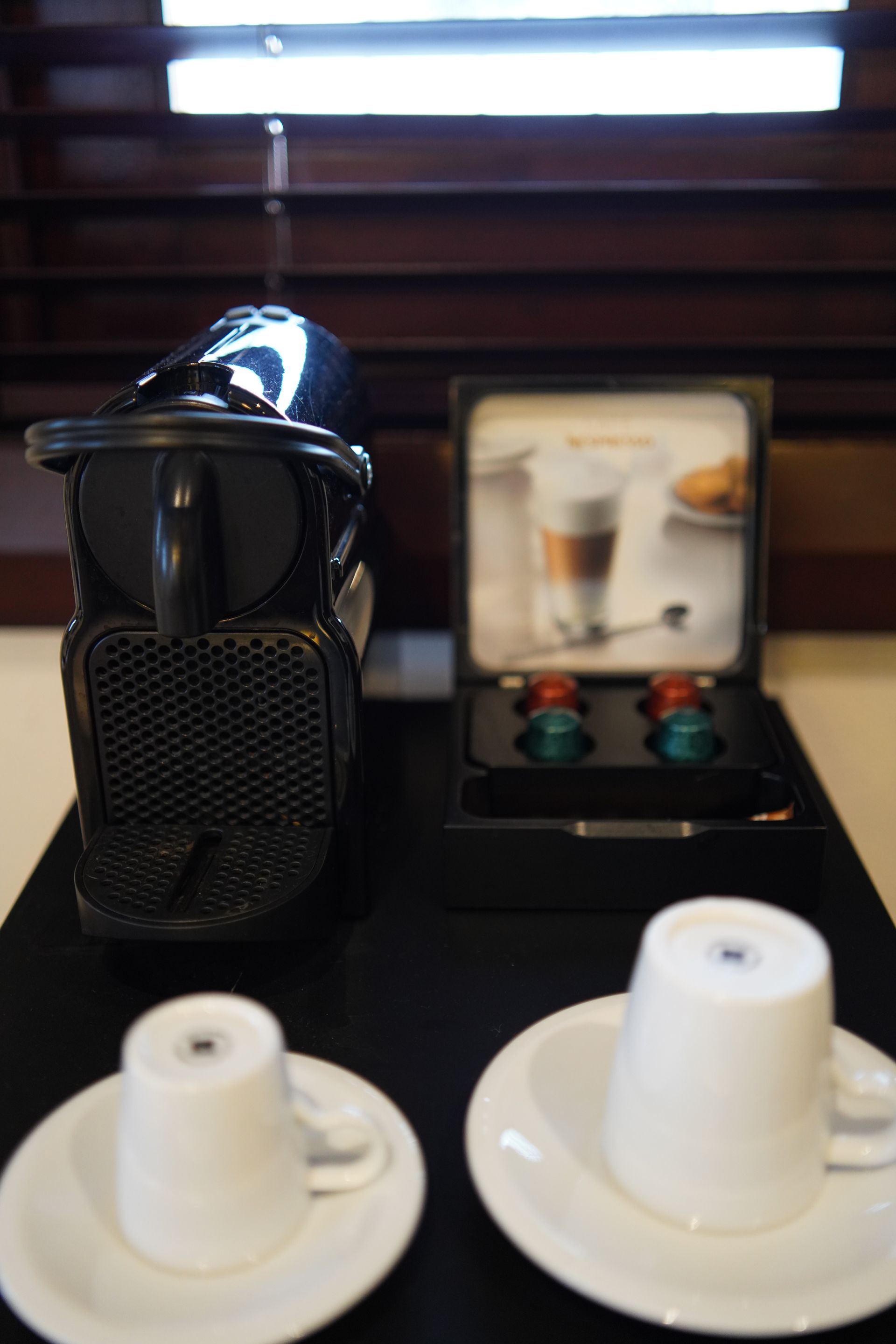 A nespresso machine sits next to two cups and saucers