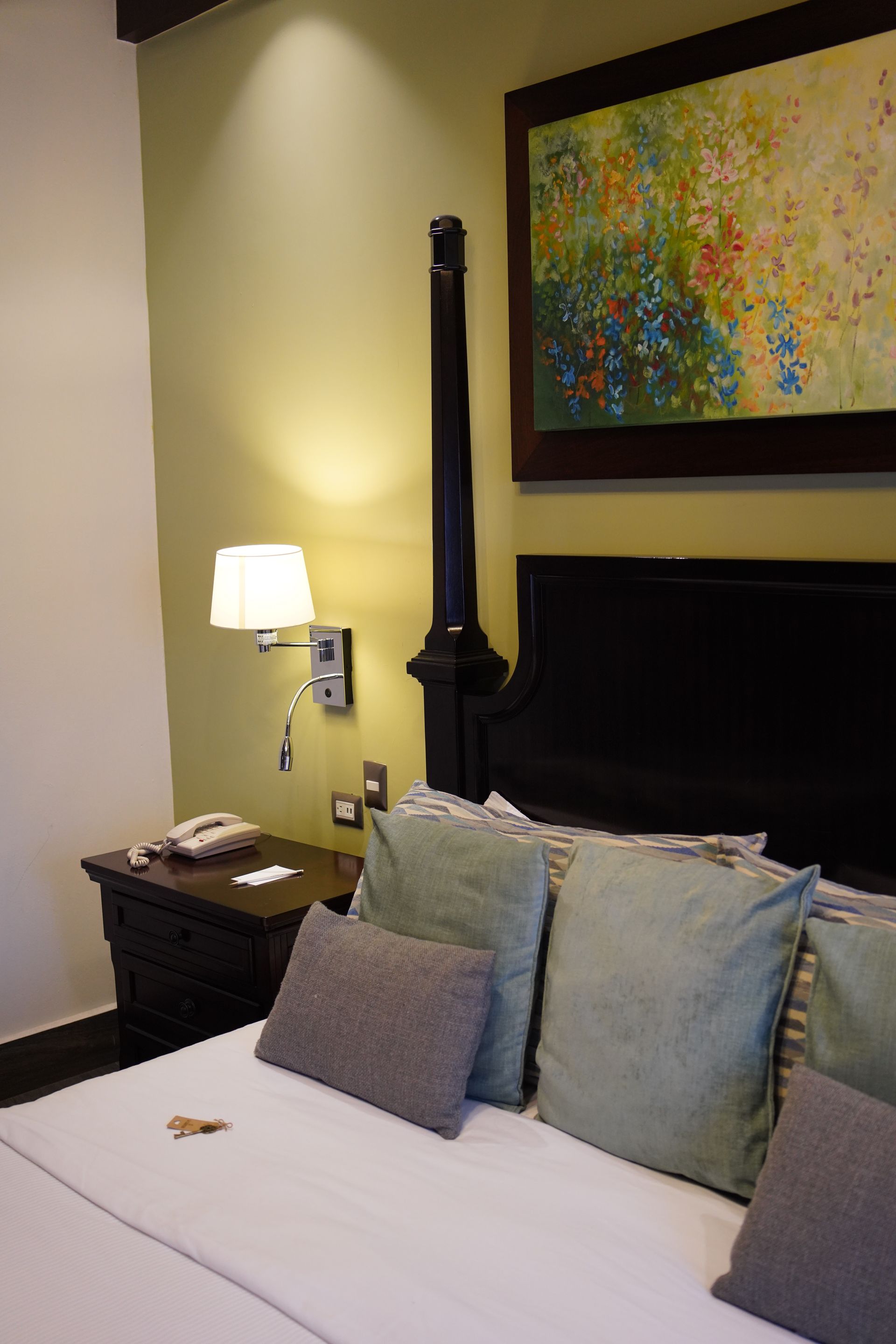 A hotel room with a bed , nightstand , lamp and painting on the wall