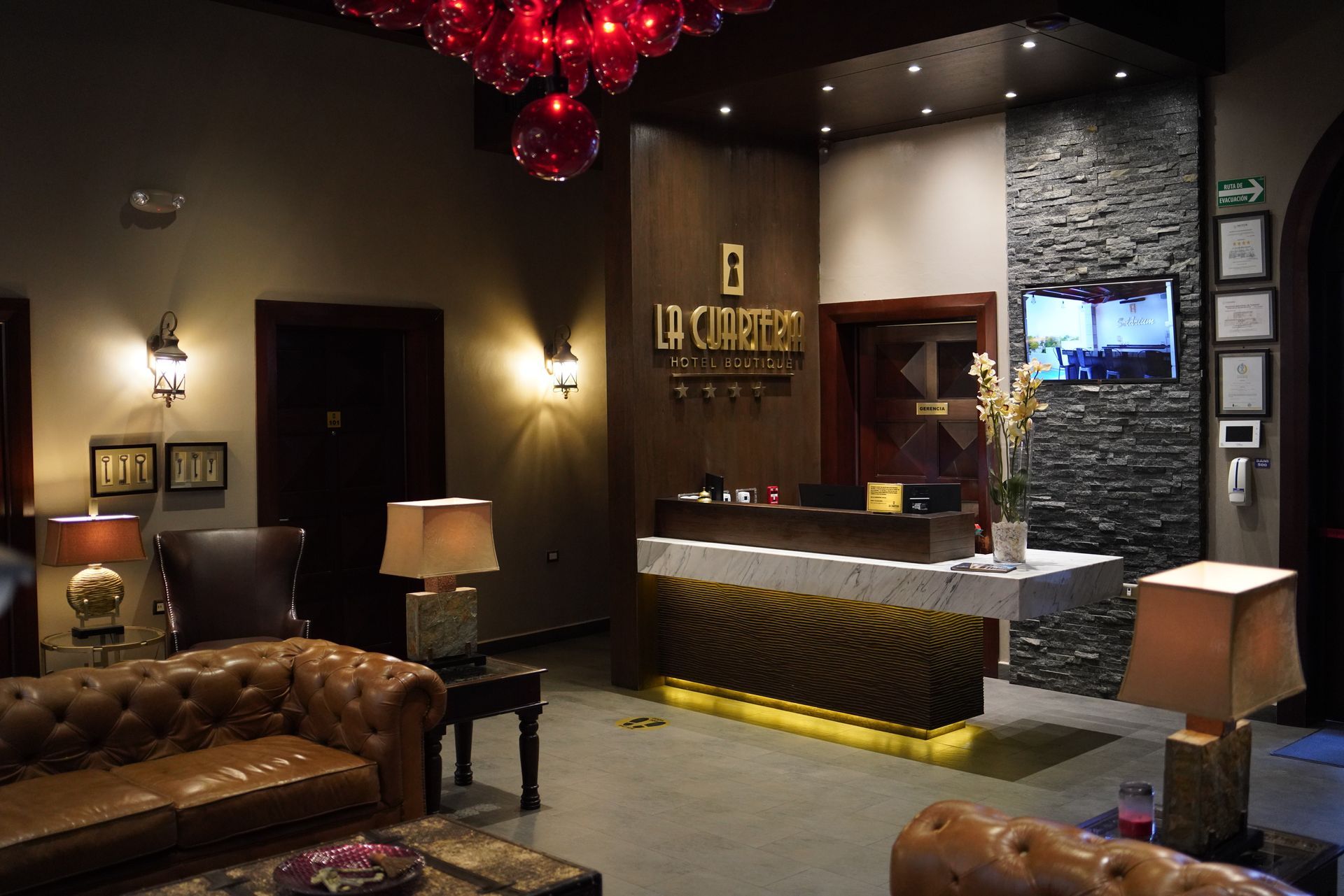 Un vestíbulo de hotel con un sofá, sillas, lámparas y un mostrador de recepción.