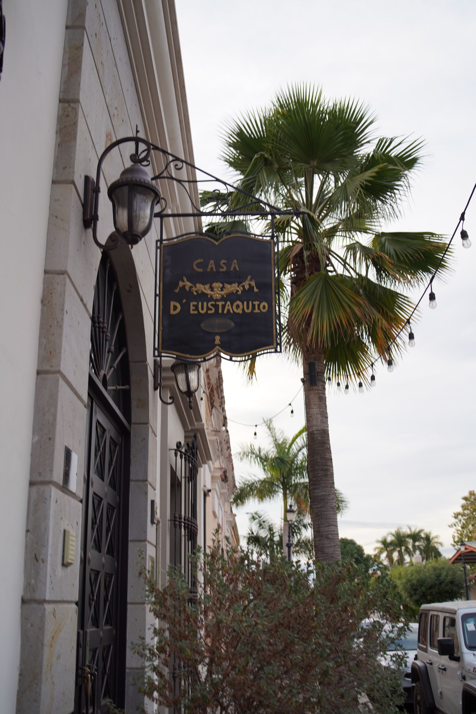 Un edificio con un cartel colgando de un costado y una palmera frente a él.