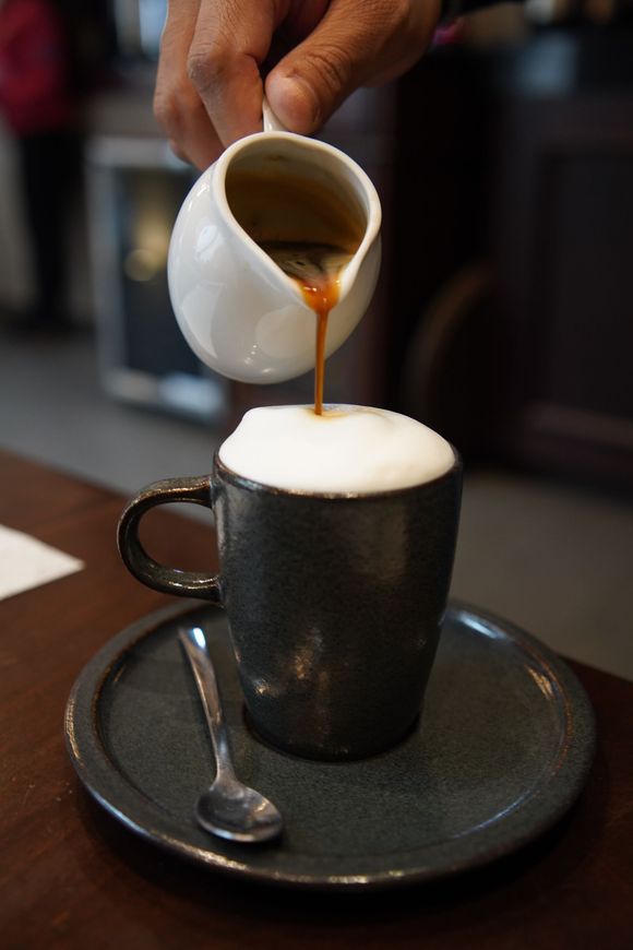 Se vierte una taza de café en un platillo con una cuchara.