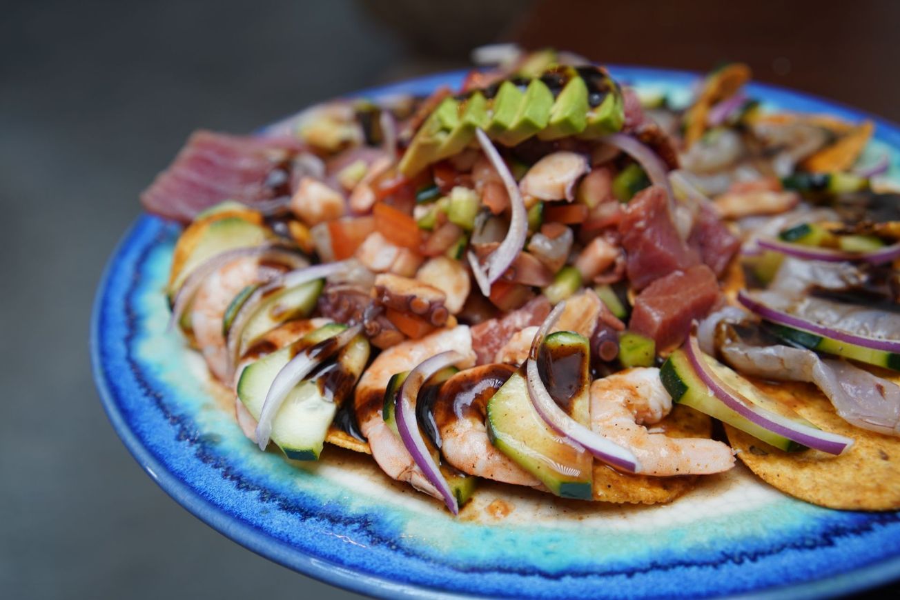 Un plato azul cubierto con una ensalada de camarones, cebollas y aguacate.
