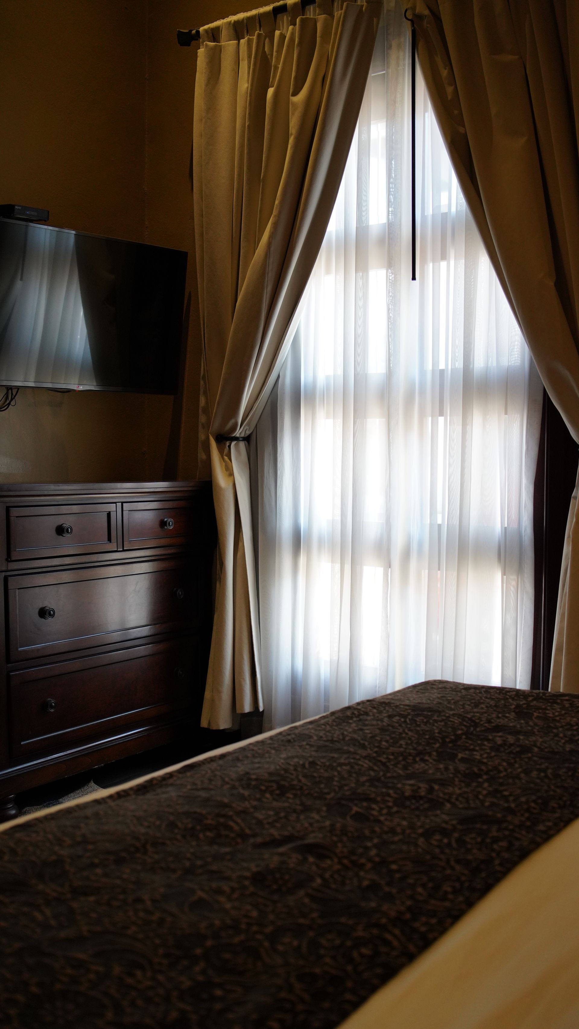 A bedroom with a bed , dresser , television and window.