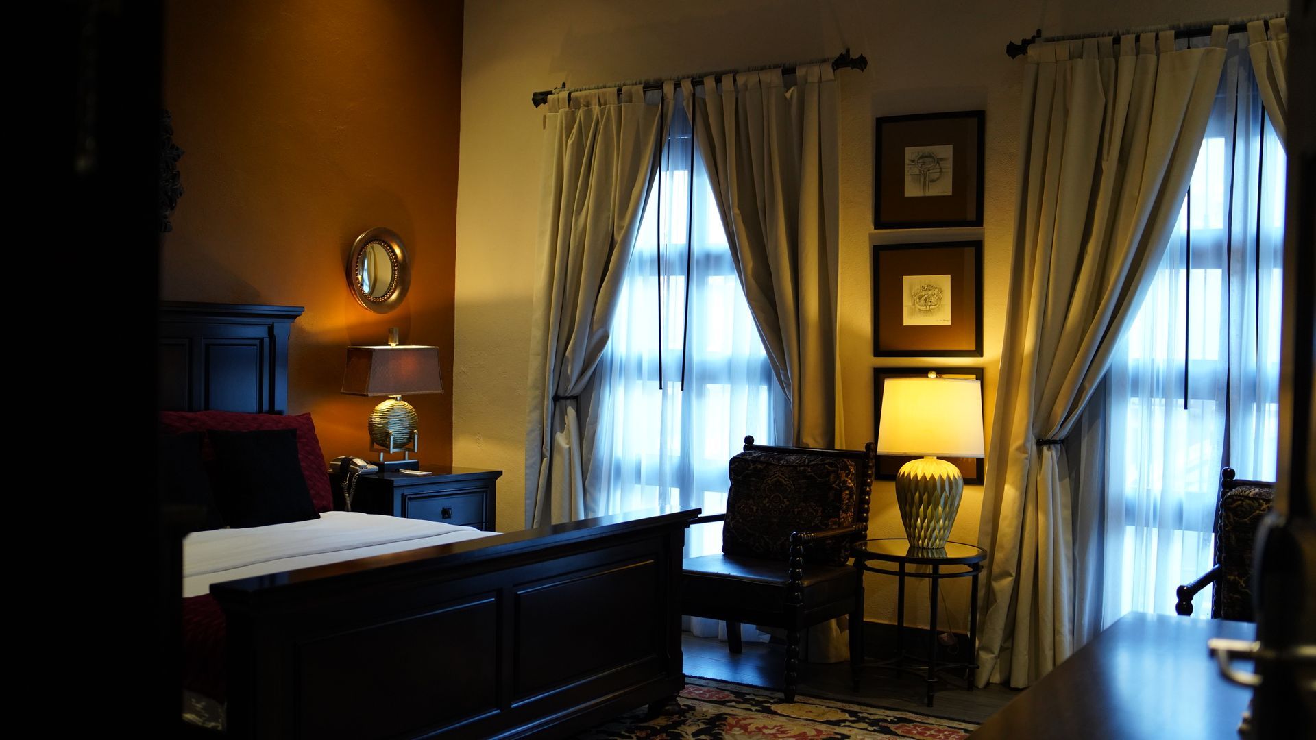 A bedroom with a bed , chairs , lamps and curtains