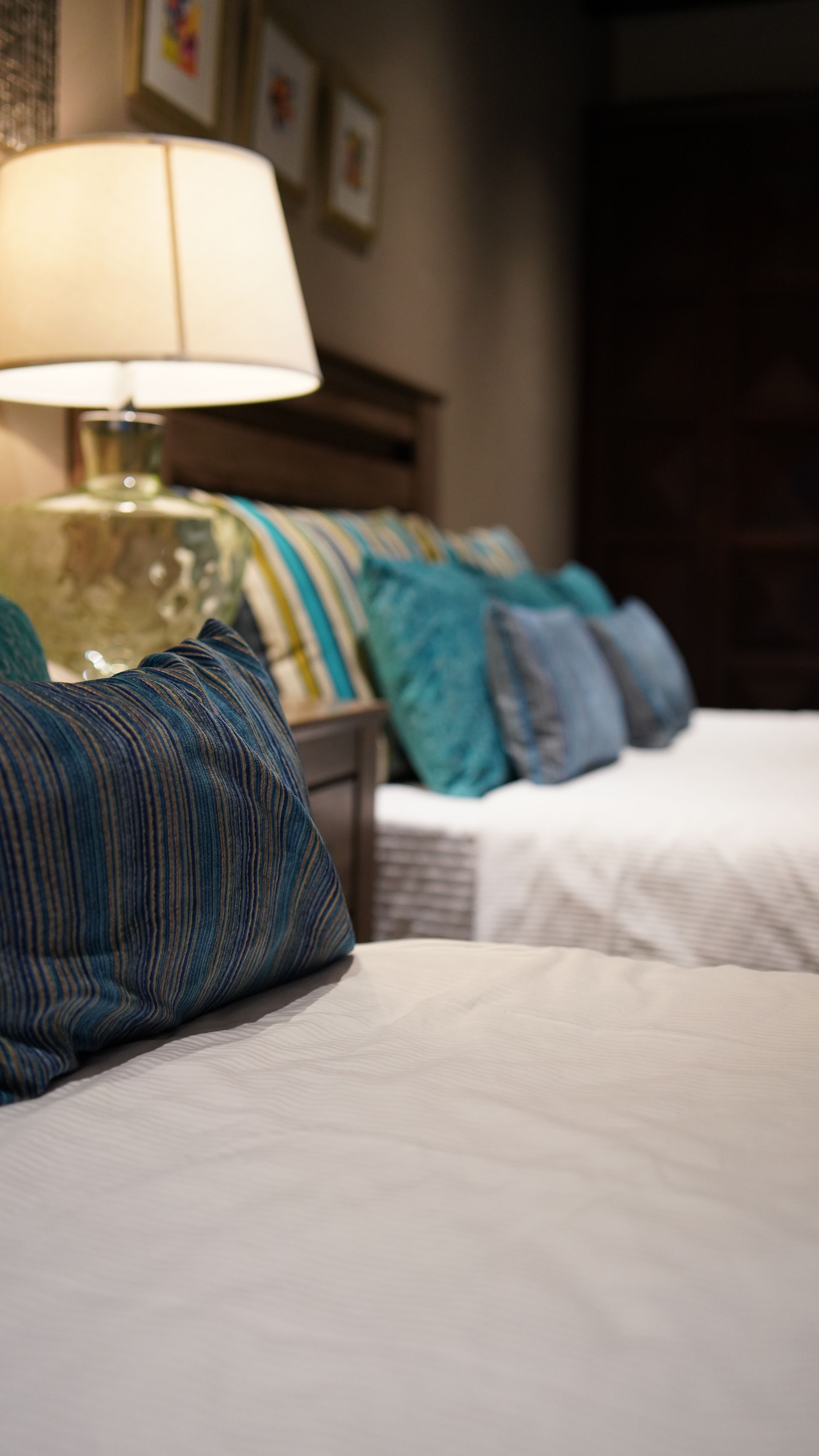 A bedroom with two beds , a lamp , and blue pillows.