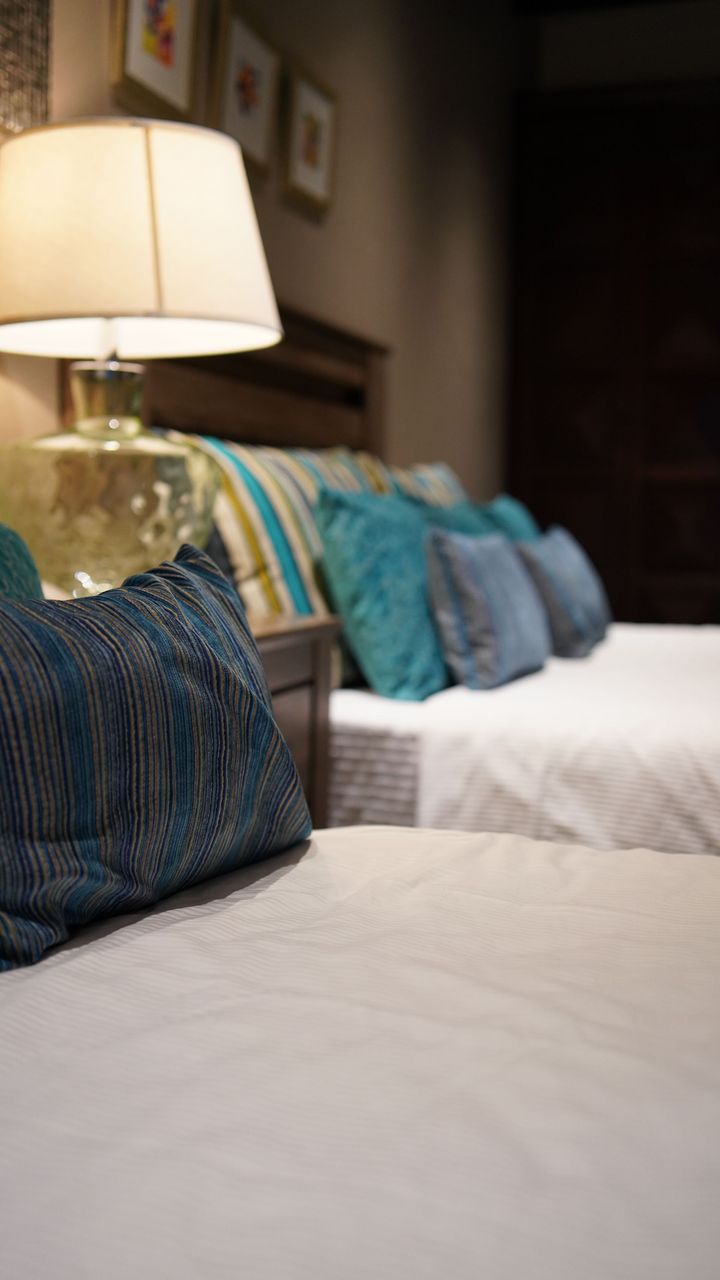 Un dormitorio con dos camas, una lámpara y almohadas azules.