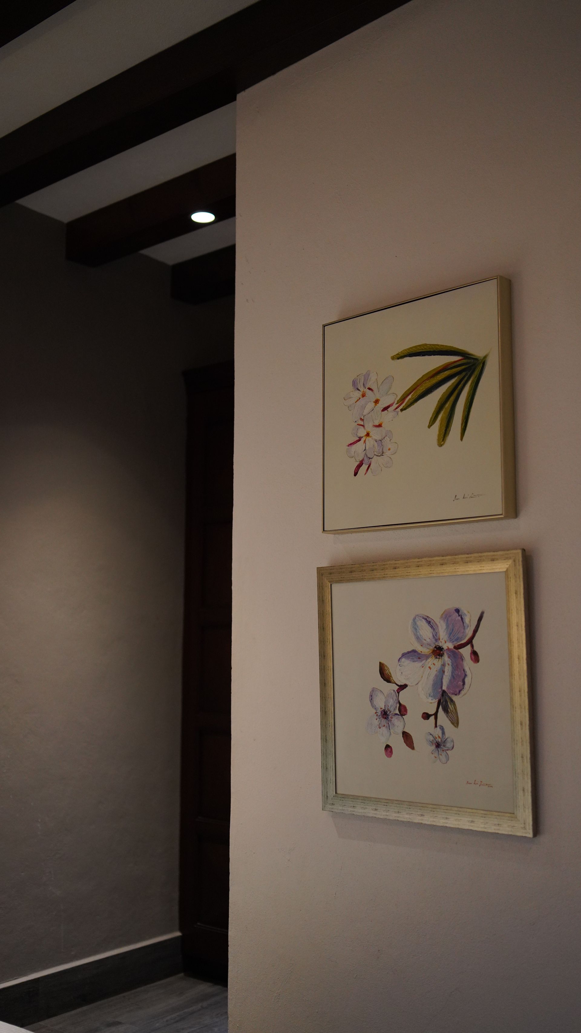 Two paintings of flowers are hanging on a wall in a hallway.