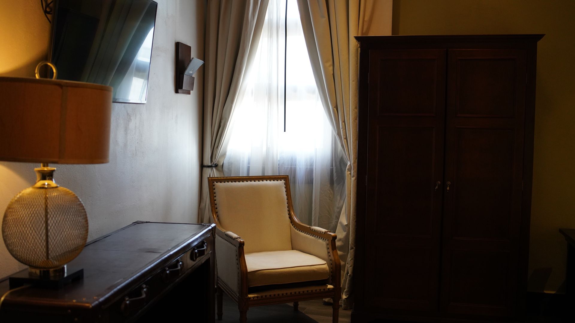 A room with a chair , desk , lamp and wardrobe.