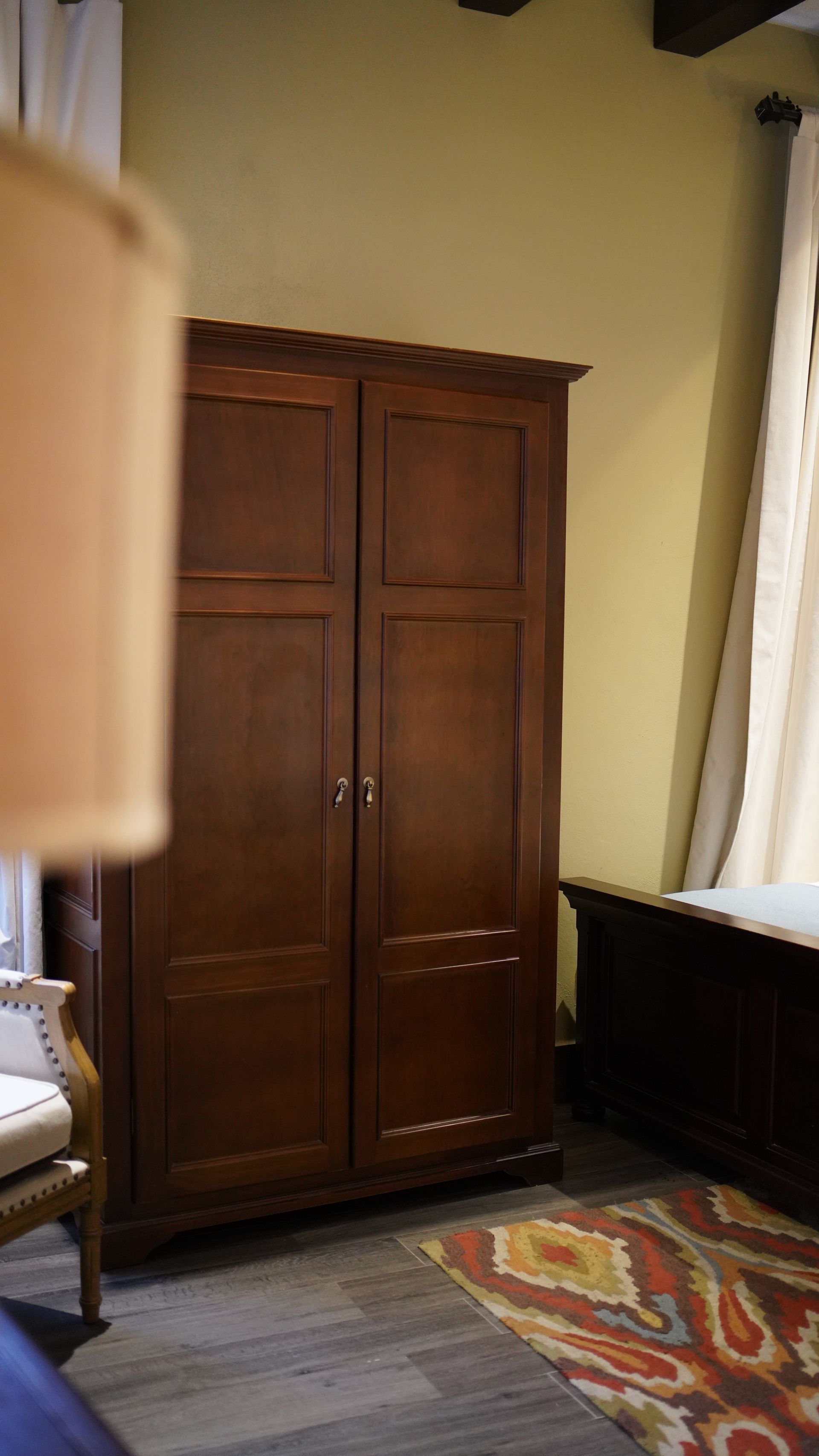 A bedroom with a large wooden wardrobe and a rug.