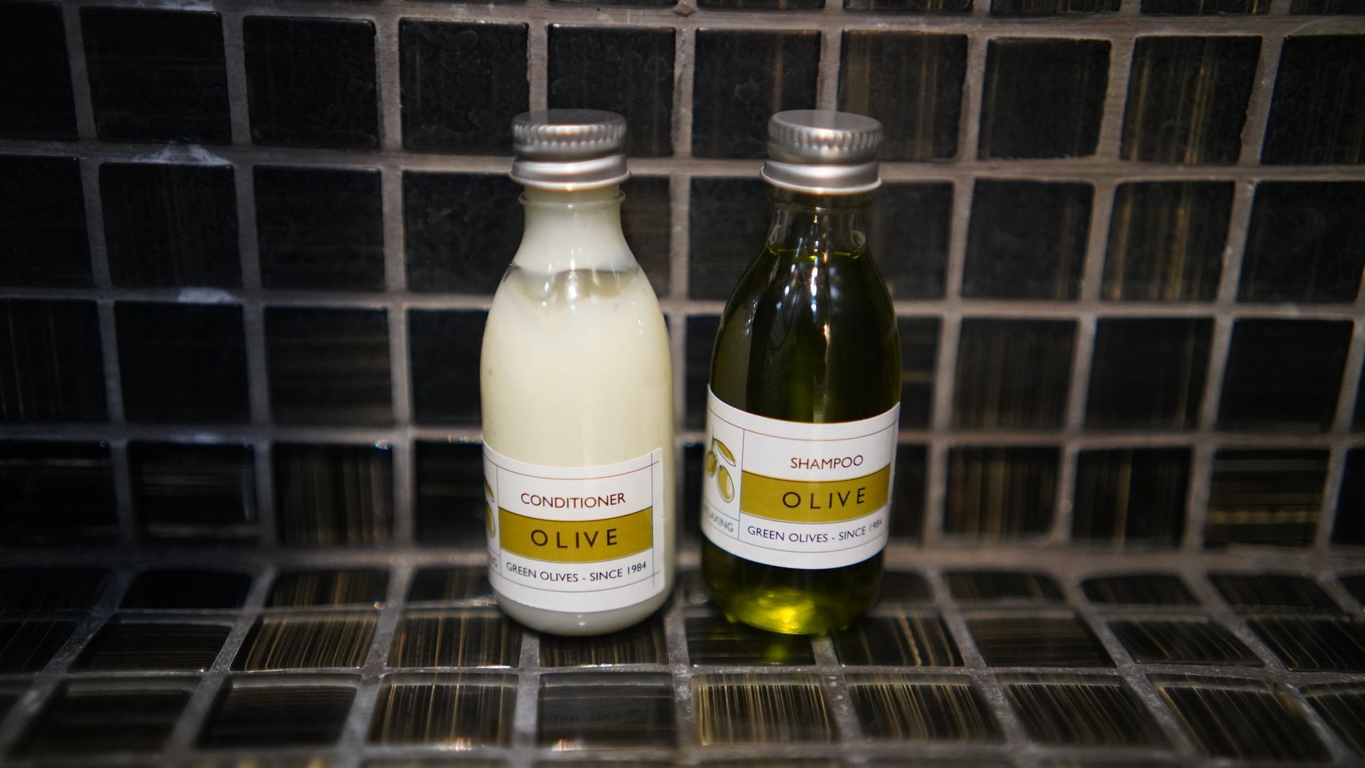 Two bottles of olive oil are sitting on a tiled floor