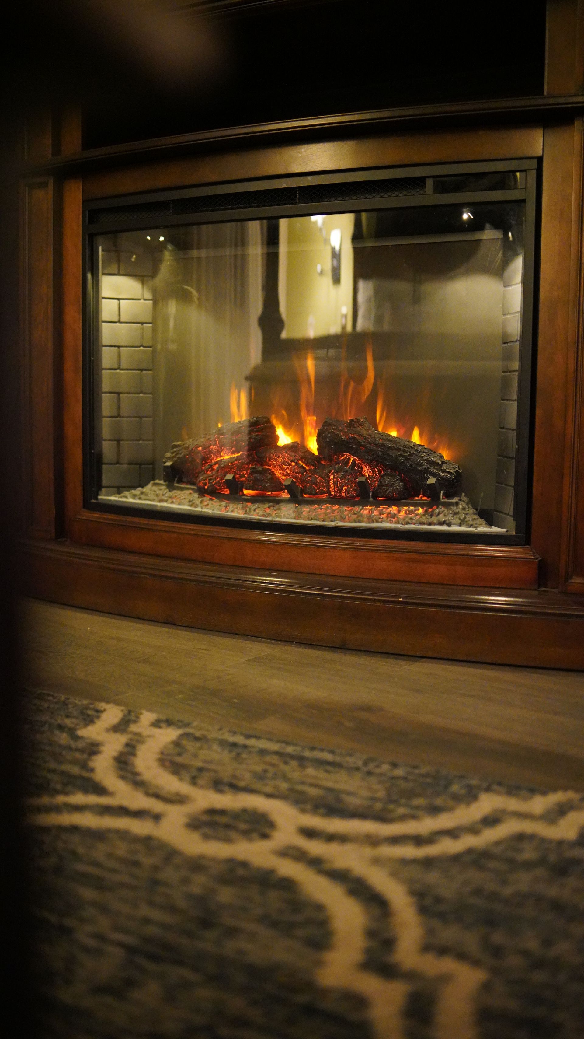 A fireplace with a rug in front of it is lit up at night.