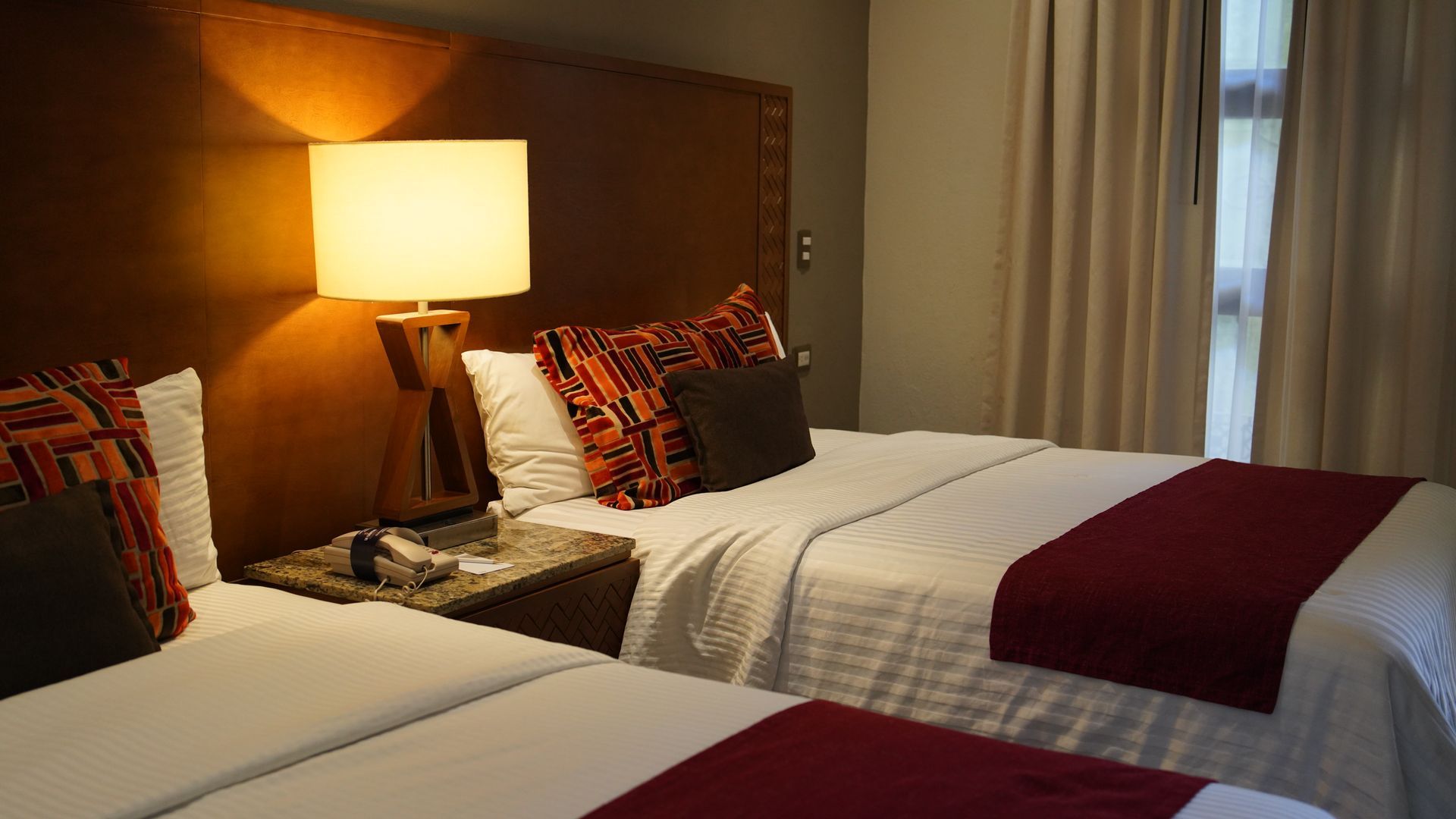 A hotel room with two beds and a lamp.