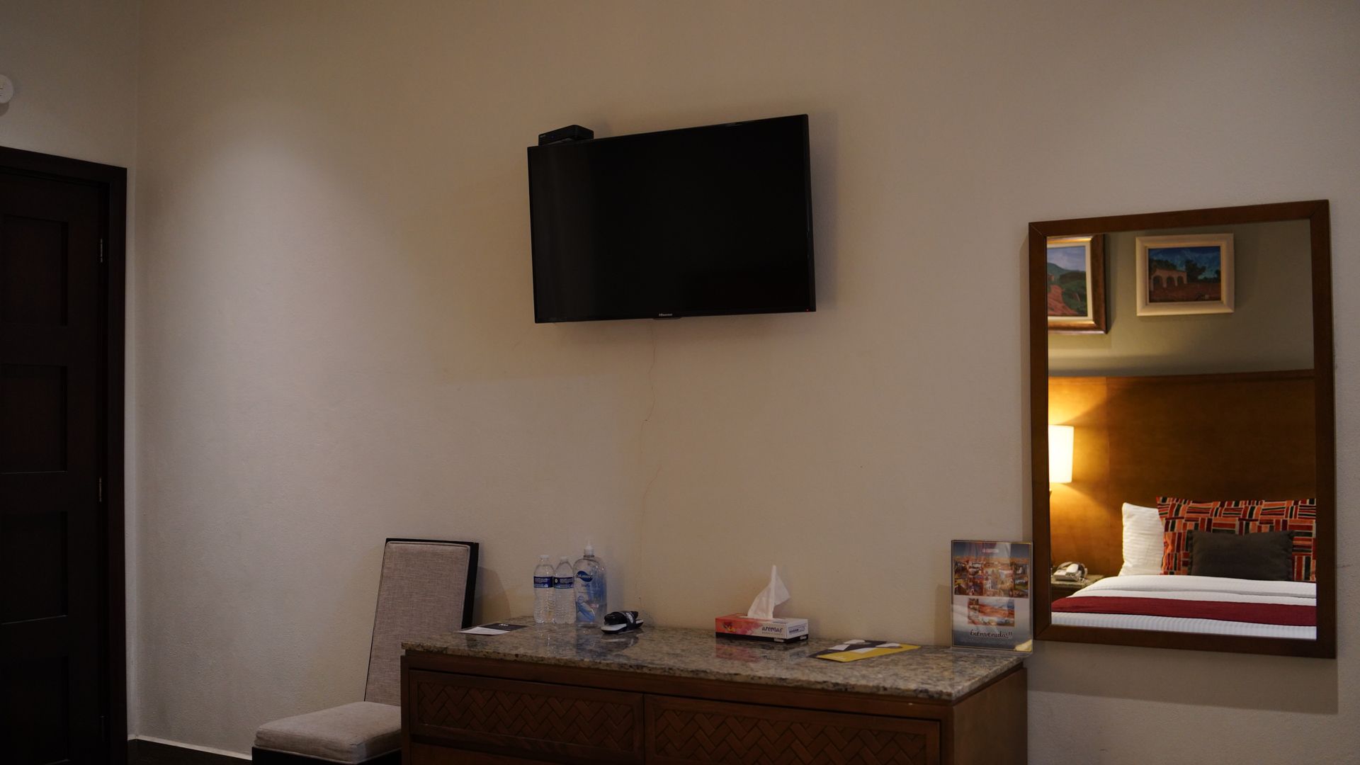 A hotel room with a television , dresser , chair and mirror.