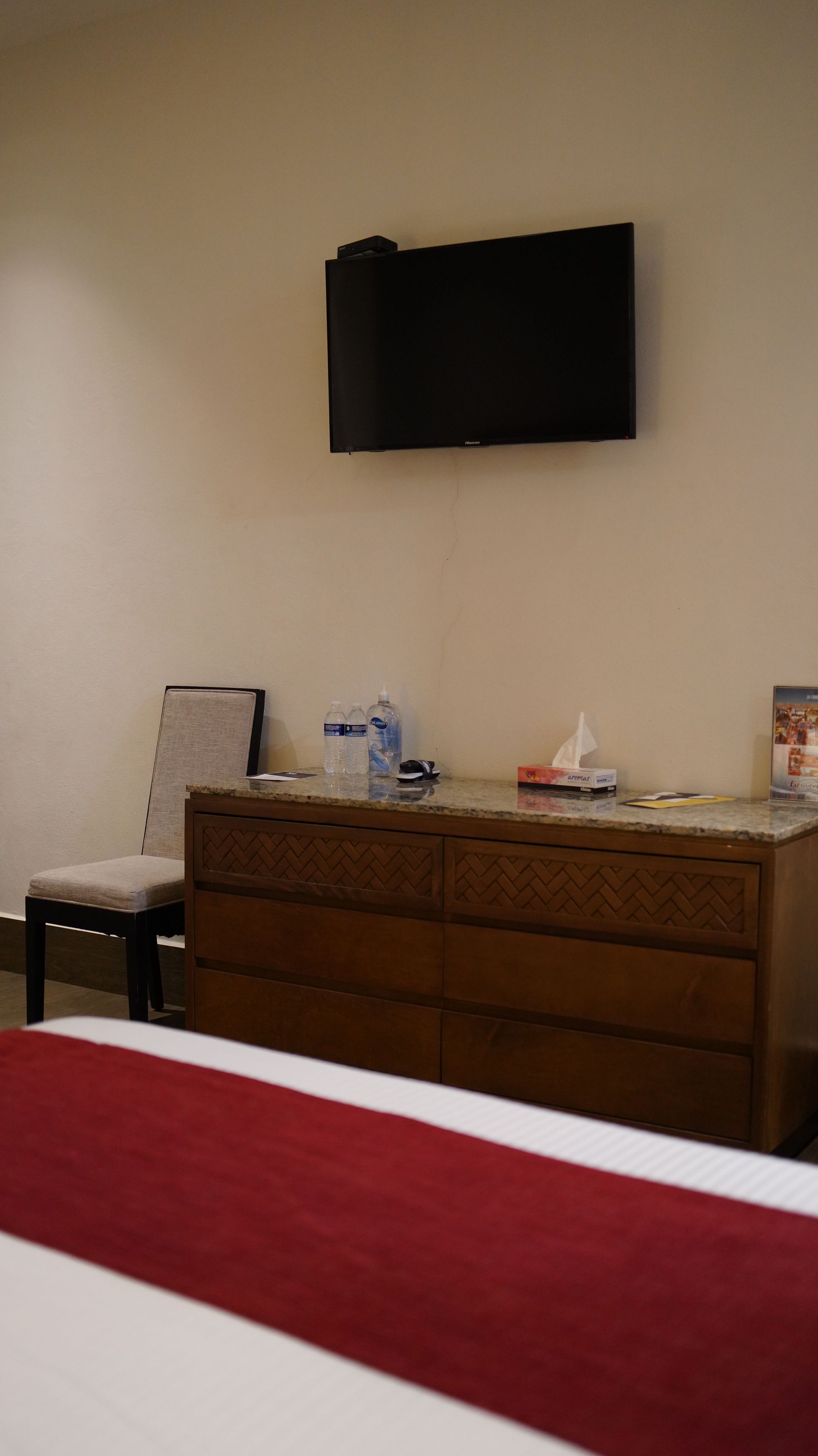 A hotel room with a bed , dresser , chair and television.