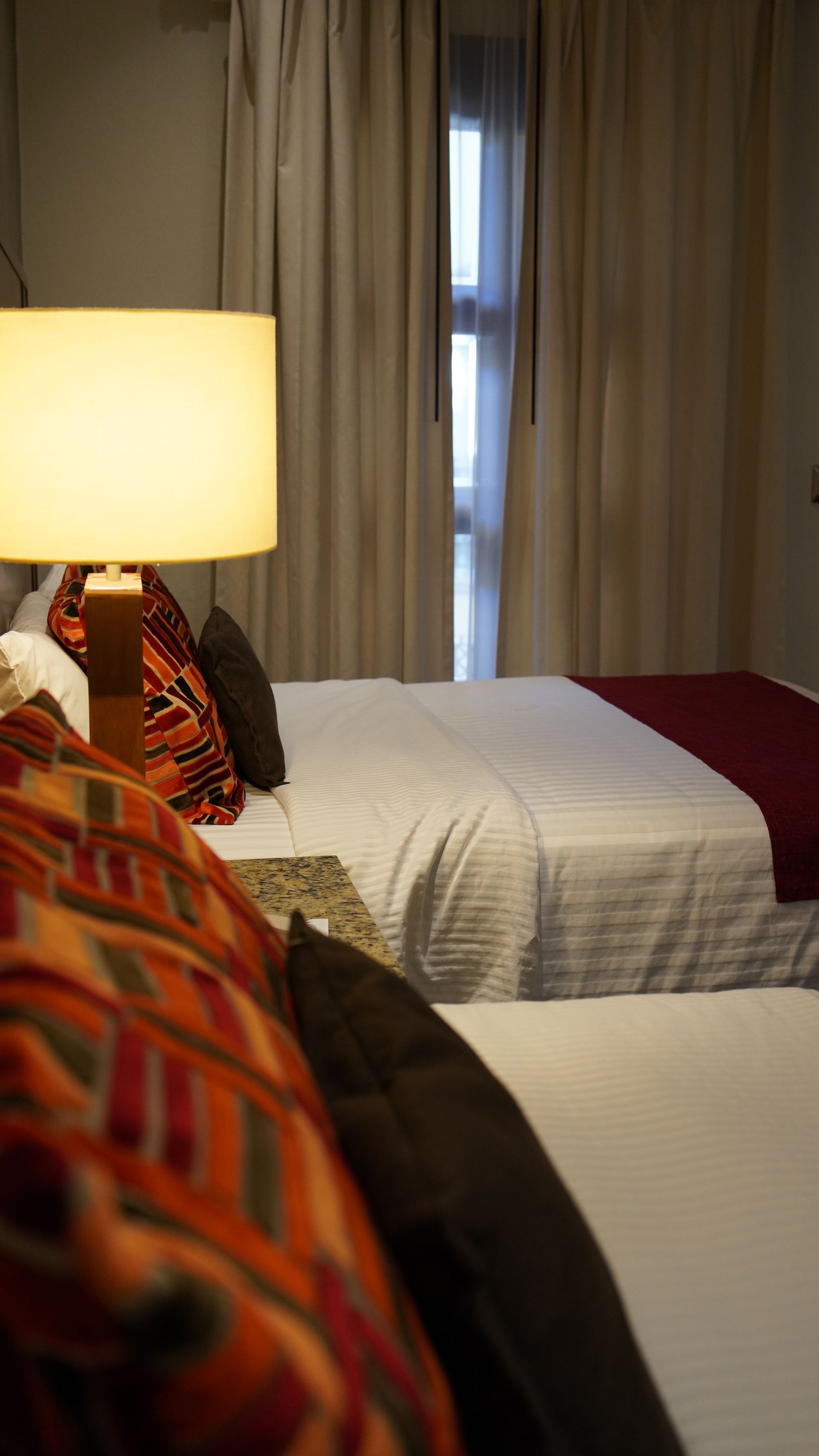 A hotel room with two beds , a lamp and a window.