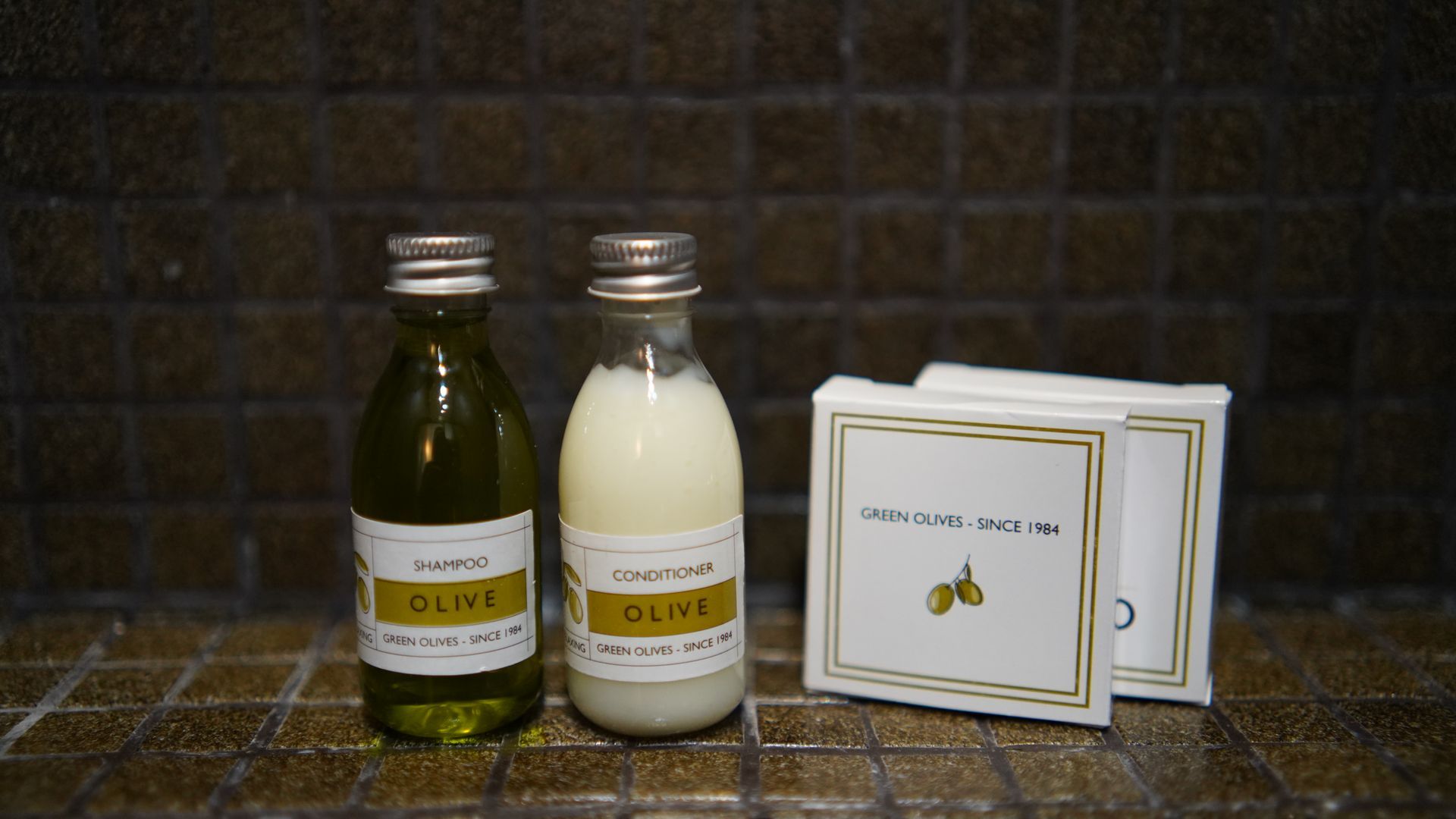 Two bottles of olive oil and soap are on a tiled floor