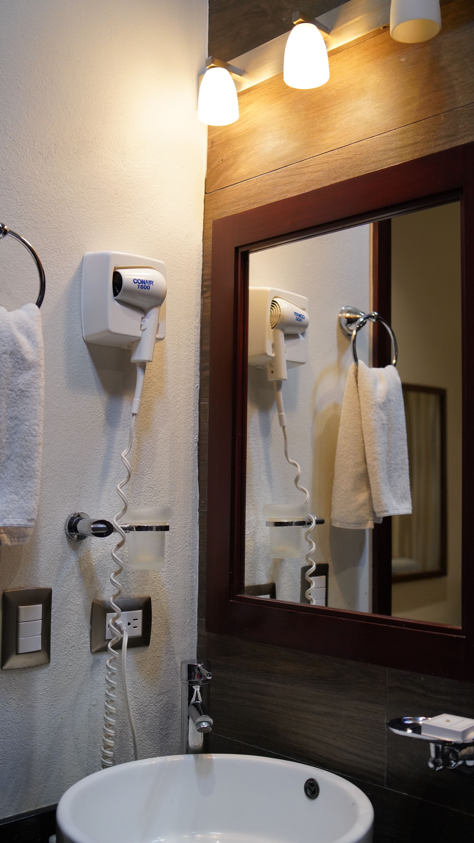 A bathroom with a sink , mirror and hair dryers