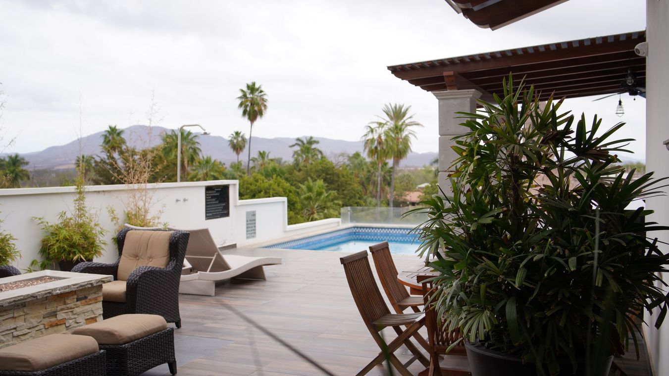 Un patio con sillas y una piscina con montañas al fondo.