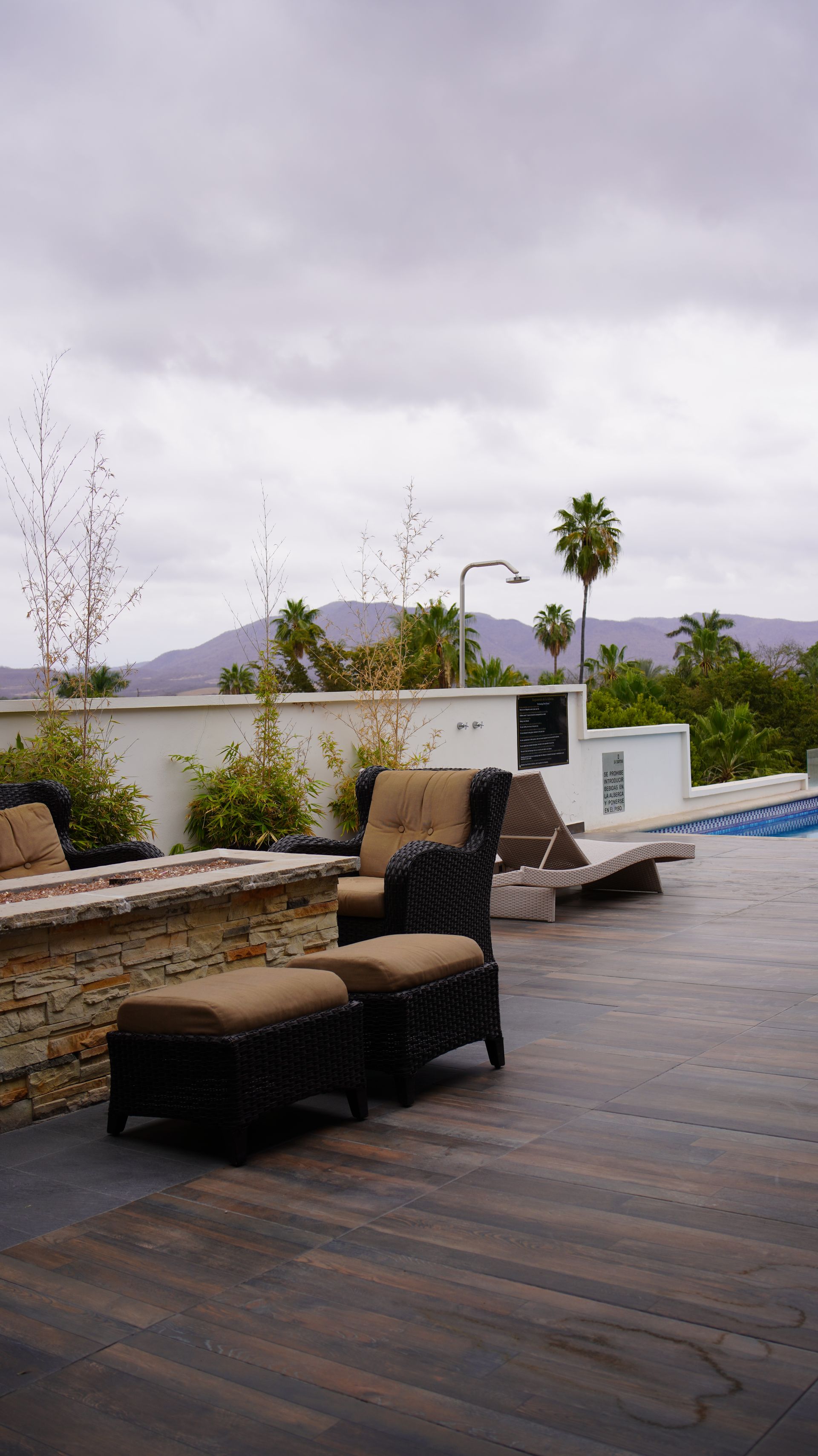 A patio with chairs and ottomans next to a pool on a cloudy day.